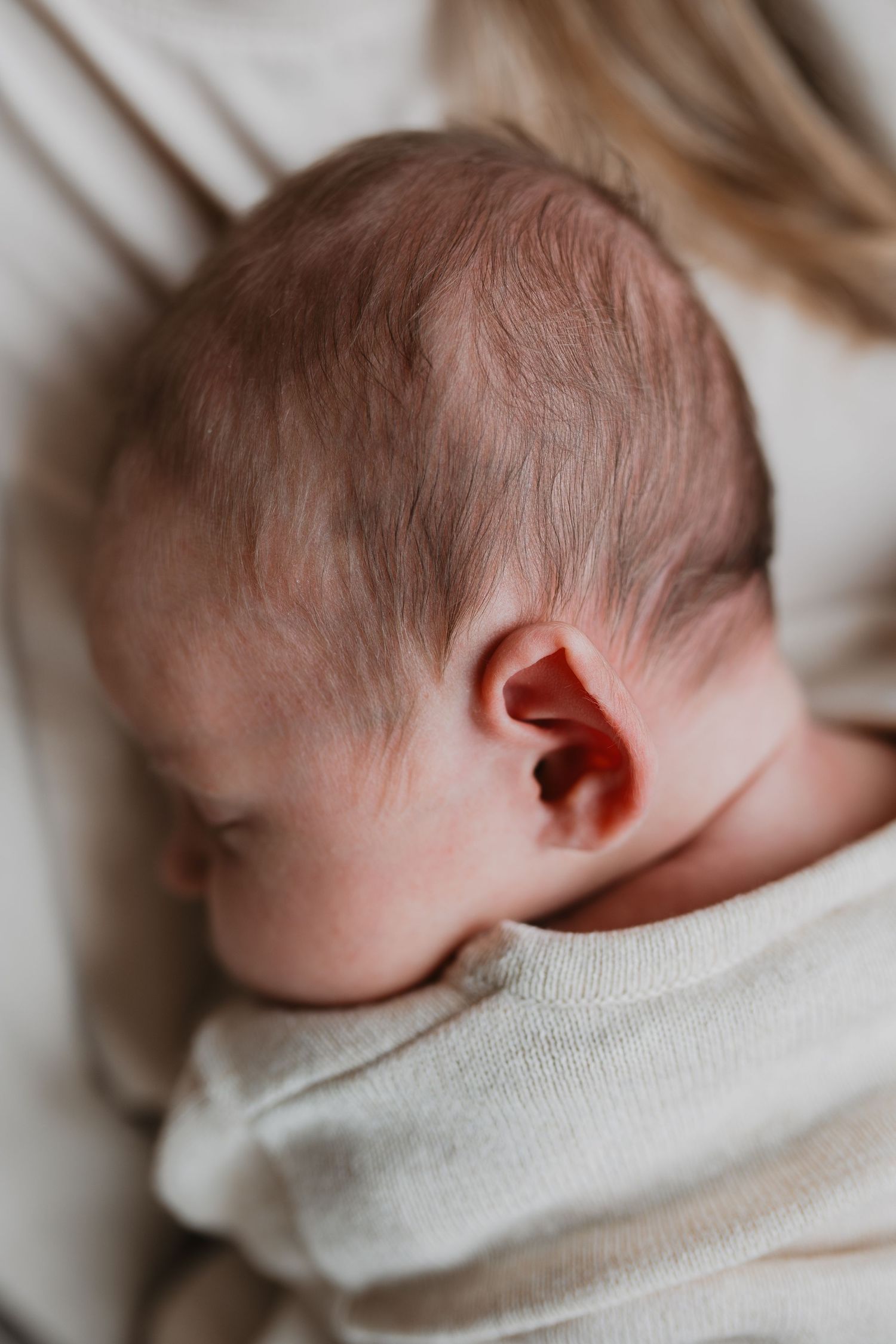 Close up van een oortje van een slapende baby. Van opzij gefotografeerd met focus op de haartjes en het kleine oortje.