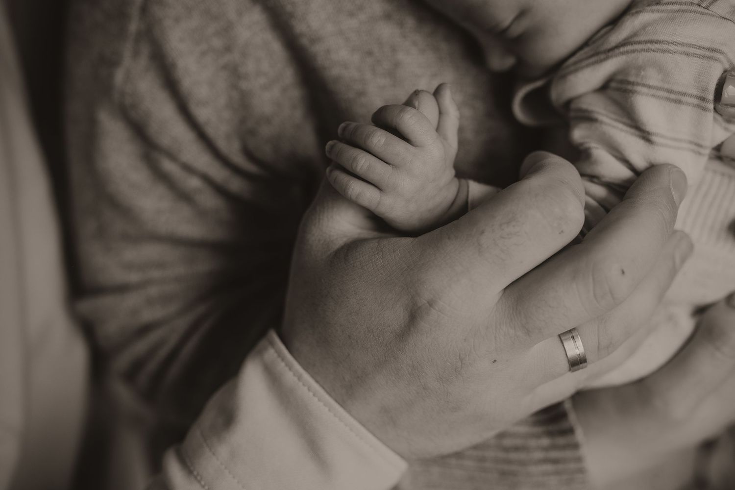 Close up beeld van de achterkant van een hand, waarvan de duim wordt vastgehouden door een newborn/baby.