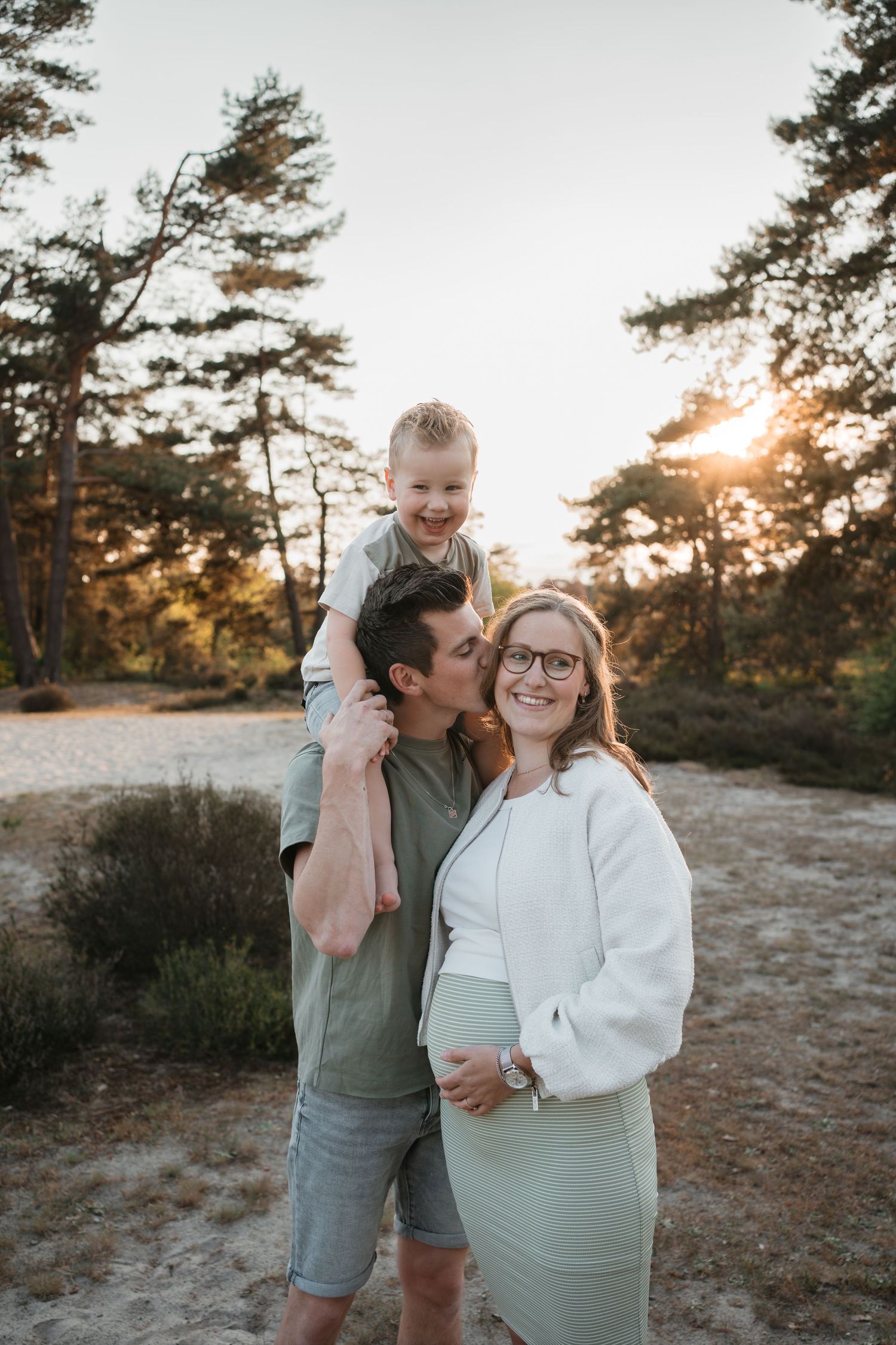 Gezinsshoot in de duinen van Soest van een zwangere vrouw en haar man die haar kust en zoontje op de schouders tijdens zonsondergang.