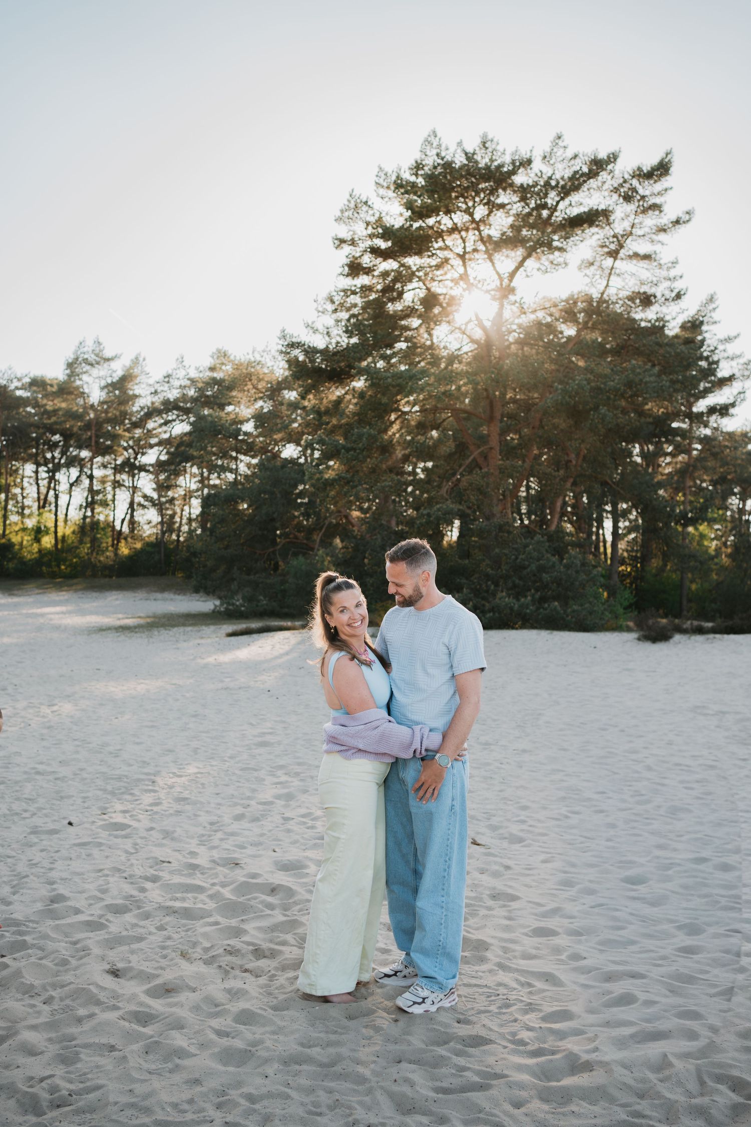 Man en vrouw poseren liefdevol tijdens een fotoshoot in de natuur. Zandvlakte met bossen in het zonlicht.