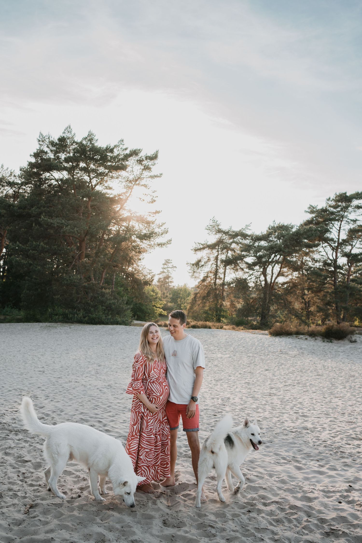 Zwangerschapsshoot Soest: aanstaande ouders poseren lachend in het zand van de Soester Duinen met hun twee witte honden.