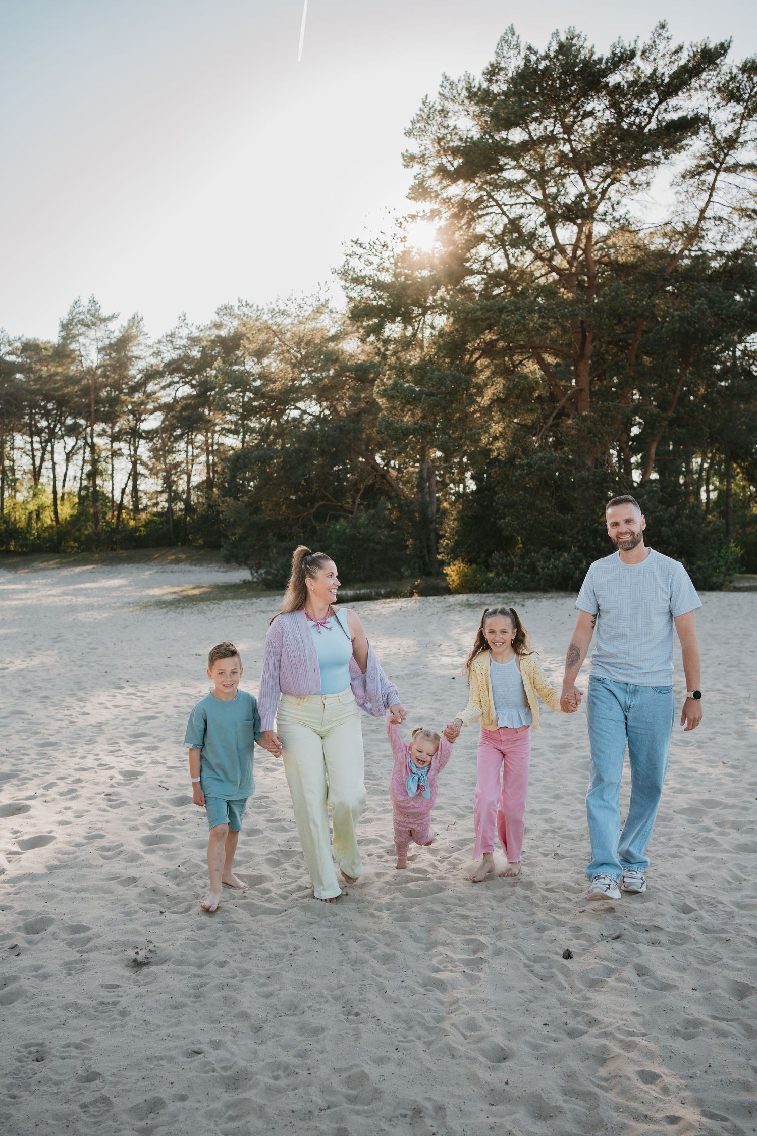 Gezinsshoot in  Soest, vrolijk kleurrijk gezin wandelt hand in hand door het zand van de Soester Duinen.