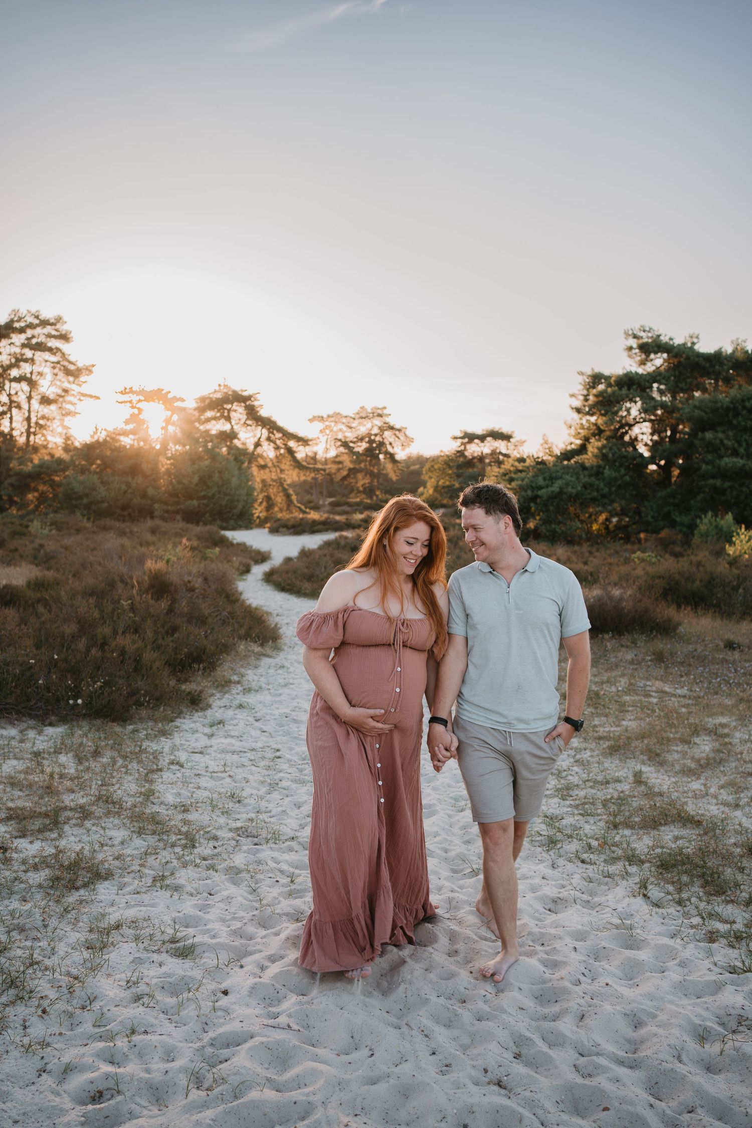 Zwangere vrouw wandelt hand in hand met haar partner door de natuur tijdens zonsondergang.