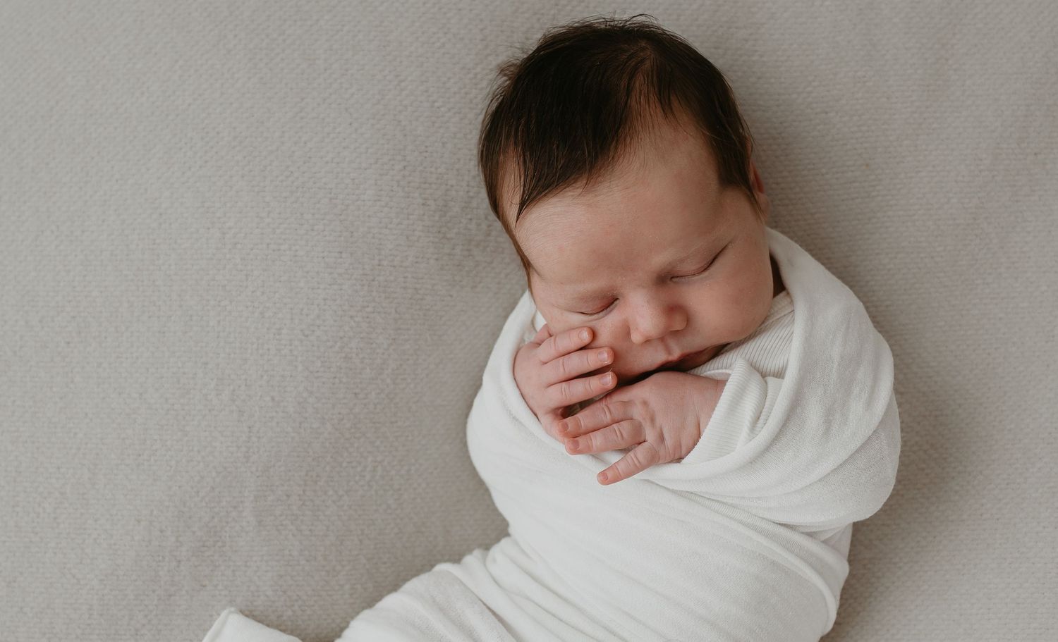 Newborn die in een doek ligt gewikkeld. De baby heeft donker haar en zijn ogen dicht.