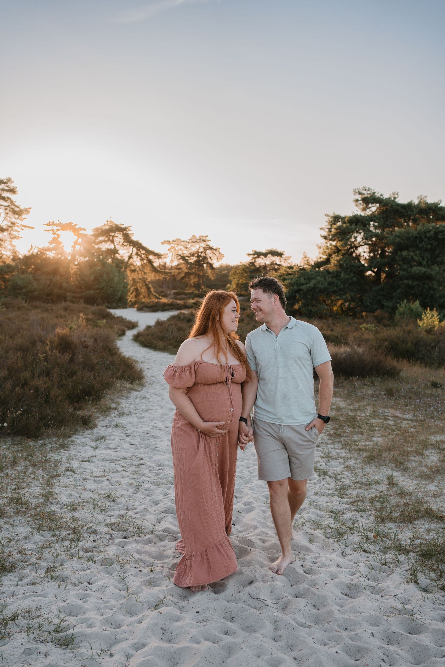 Zwangere vrouw wandelt hand in hand met haar partner door de natuur tijdens zonsondergang.
