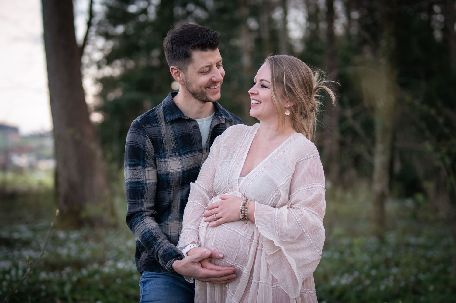 Verliebtes Paar lacht gemeinsam bei einem Fotoshooting im Wald.