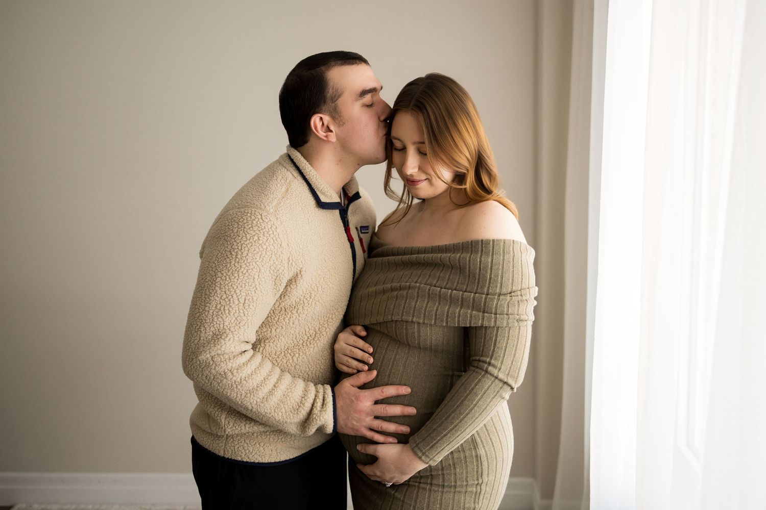 A couple in neutral tones share an intimate moment during an indoor photography session.
