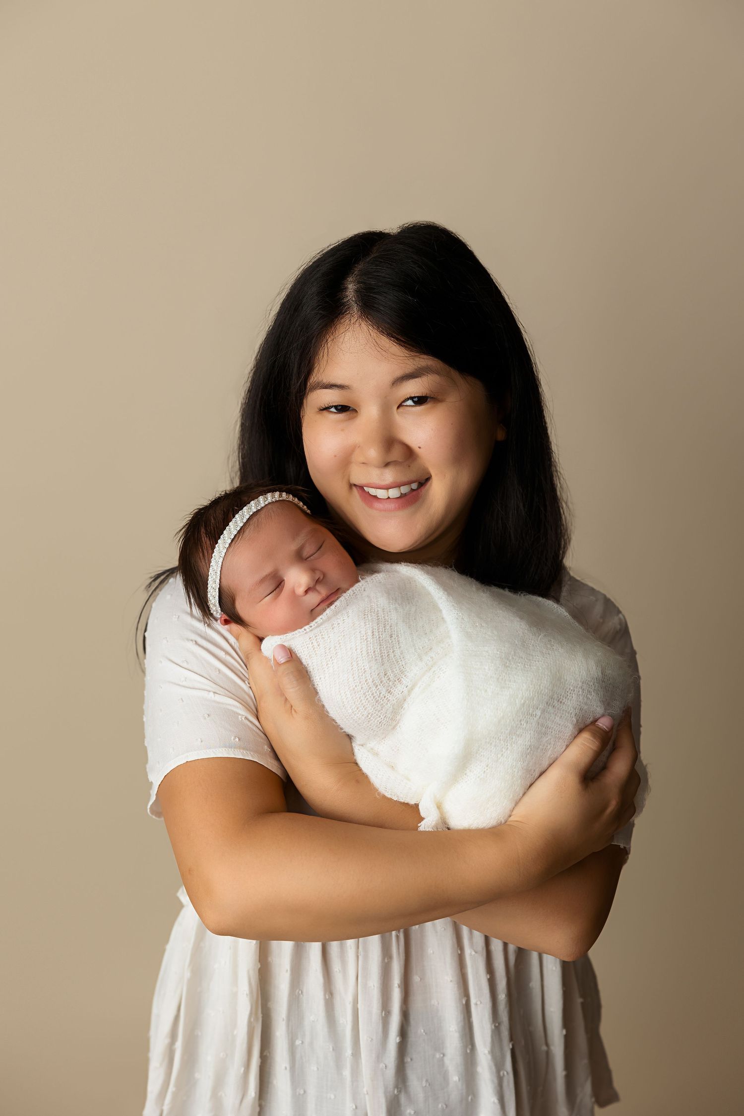 A joyful newborn portrait session against a simple beige background.