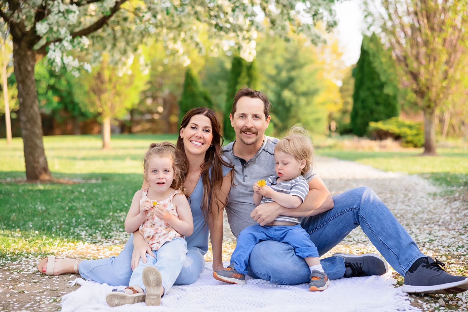 A casual outdoor family portrait on a white blanket surrounded by autumn trees.