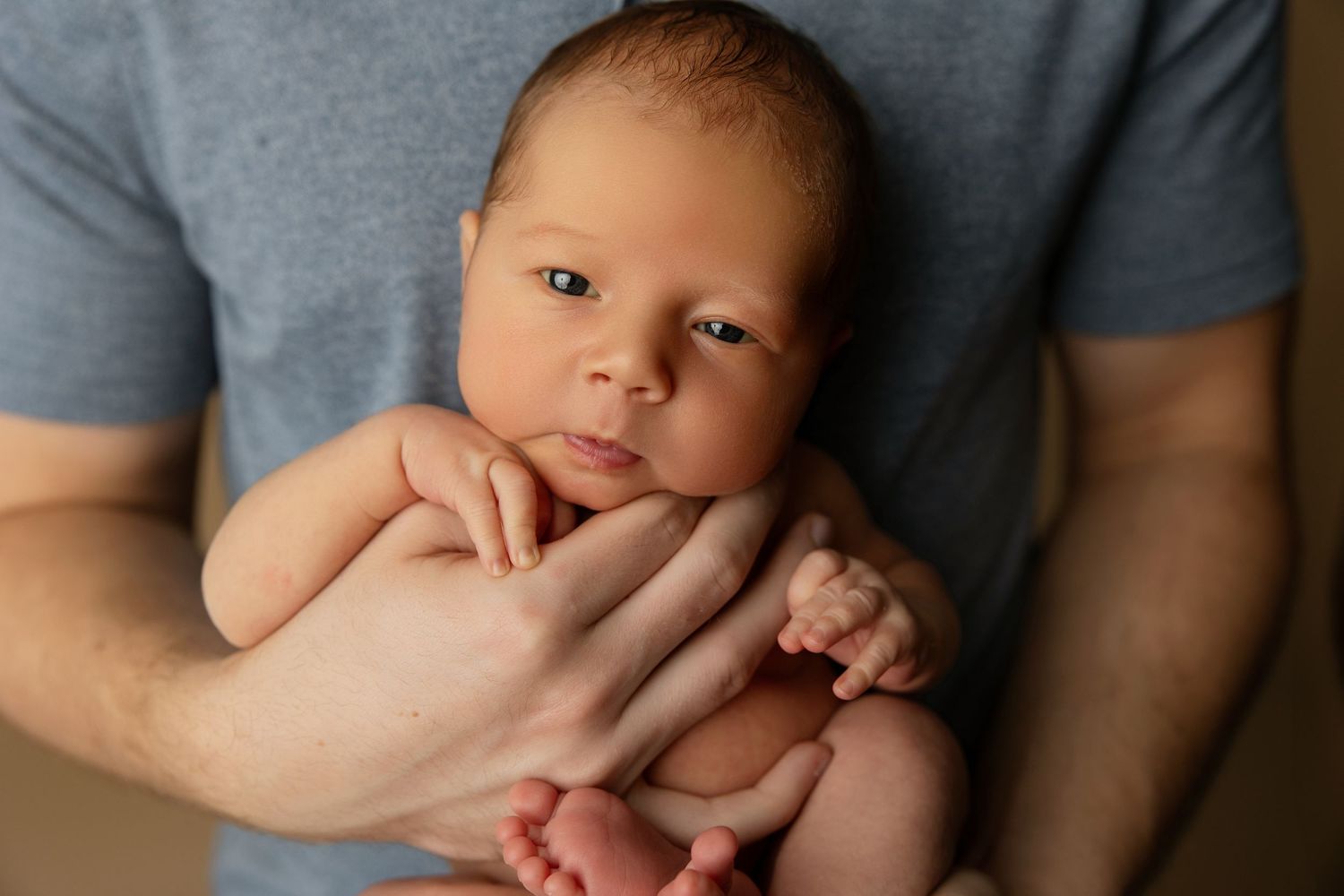 Mother in white dress holds sleeping newborn against warm brown studio backdrop.