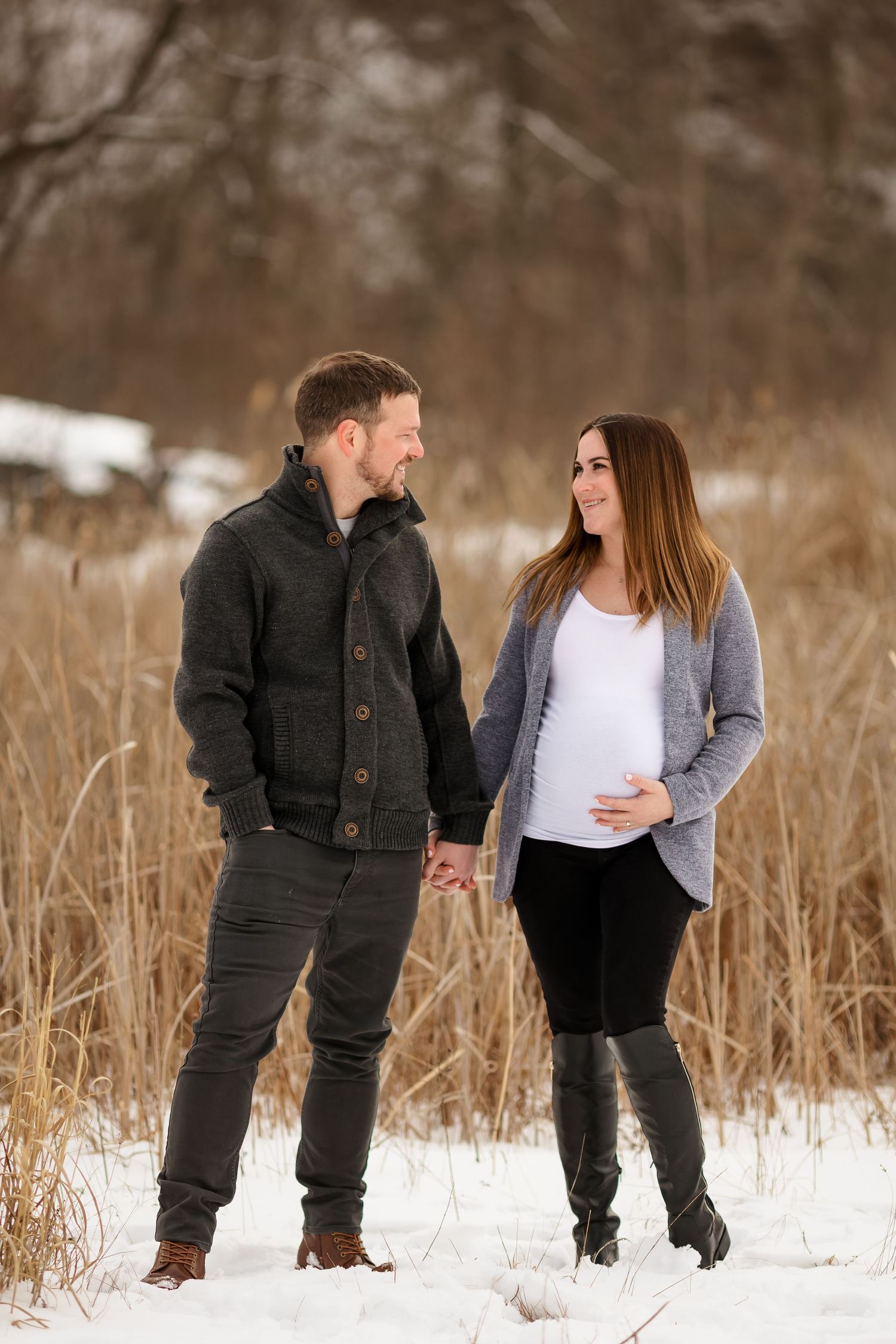 Winter maternity portrait with couple holding hands in snowy field.