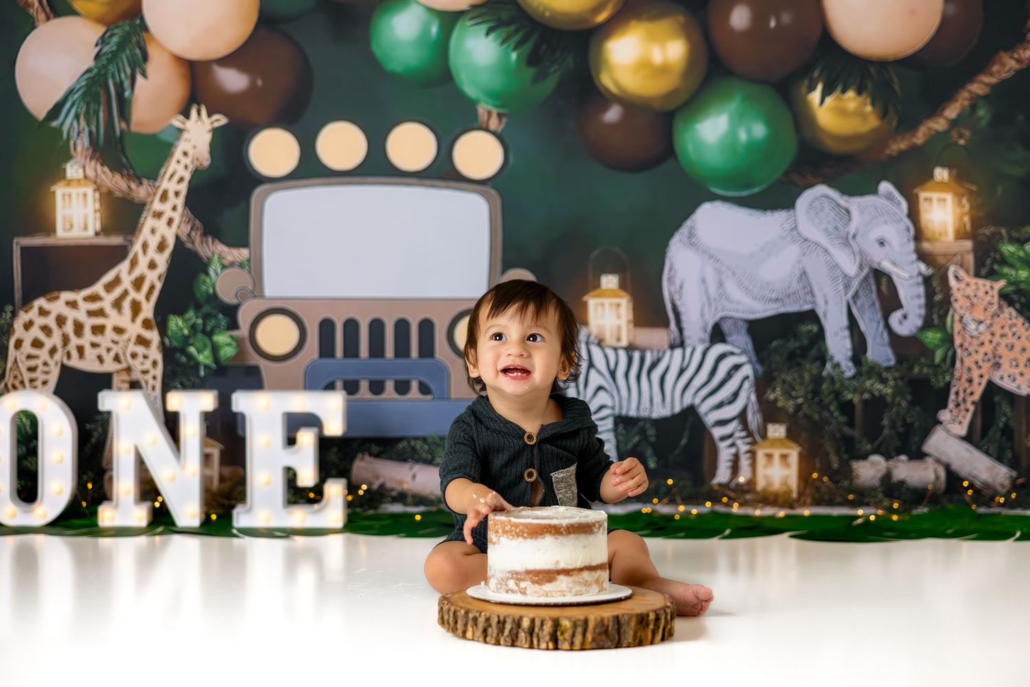Safari themed first birthday setup with green and gold balloons against a dark backdrop.