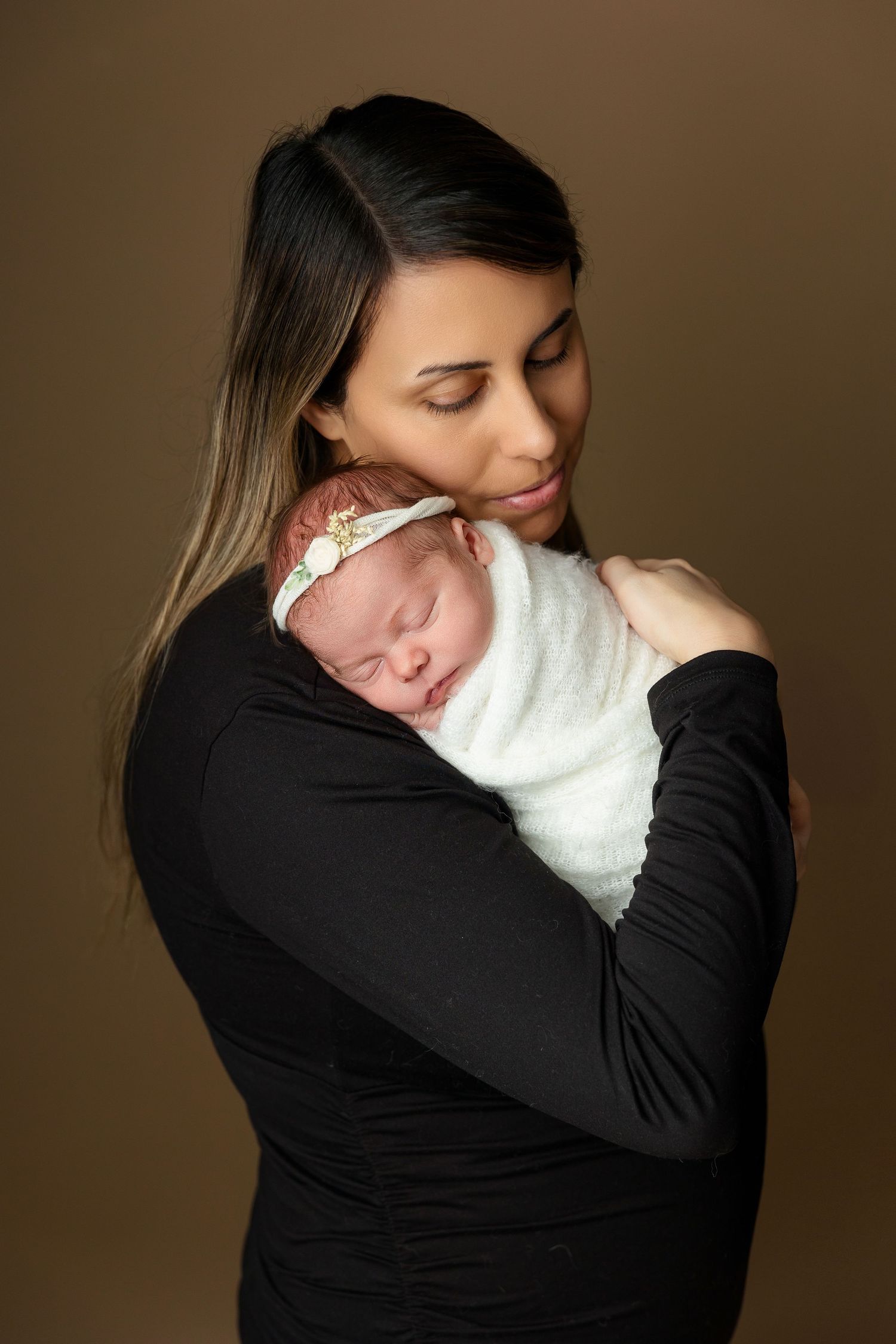 Tender moment as parent cradles sleeping newborn wrapped in white.