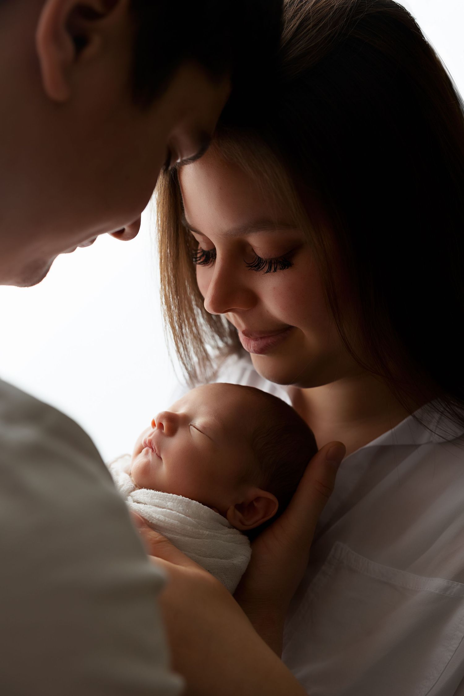 Intimate family moment with newborn baby in soft lighting against neutral background.