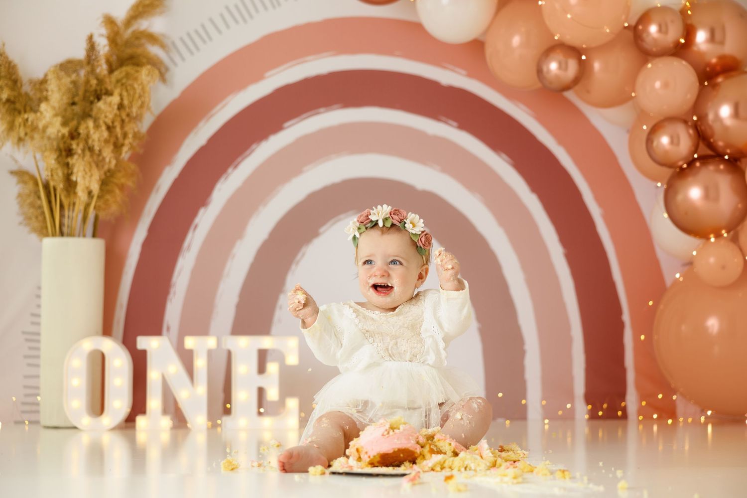 Energetic cake smash photography with vintage rainbow background and golden dried flowers.