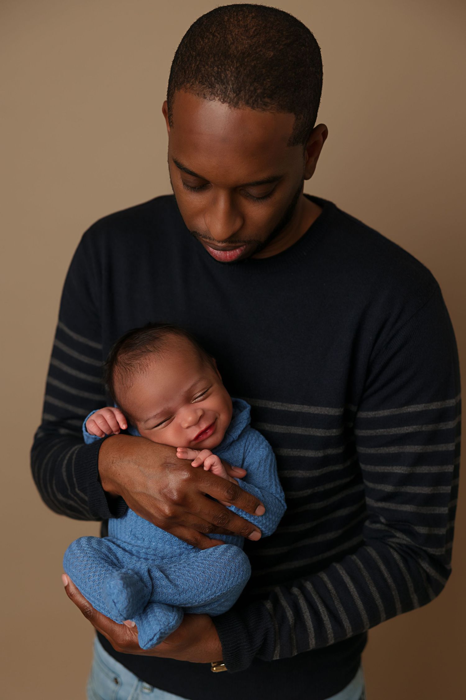 Parent in striped sweater holding sleeping baby dressed in blue knit outfit.