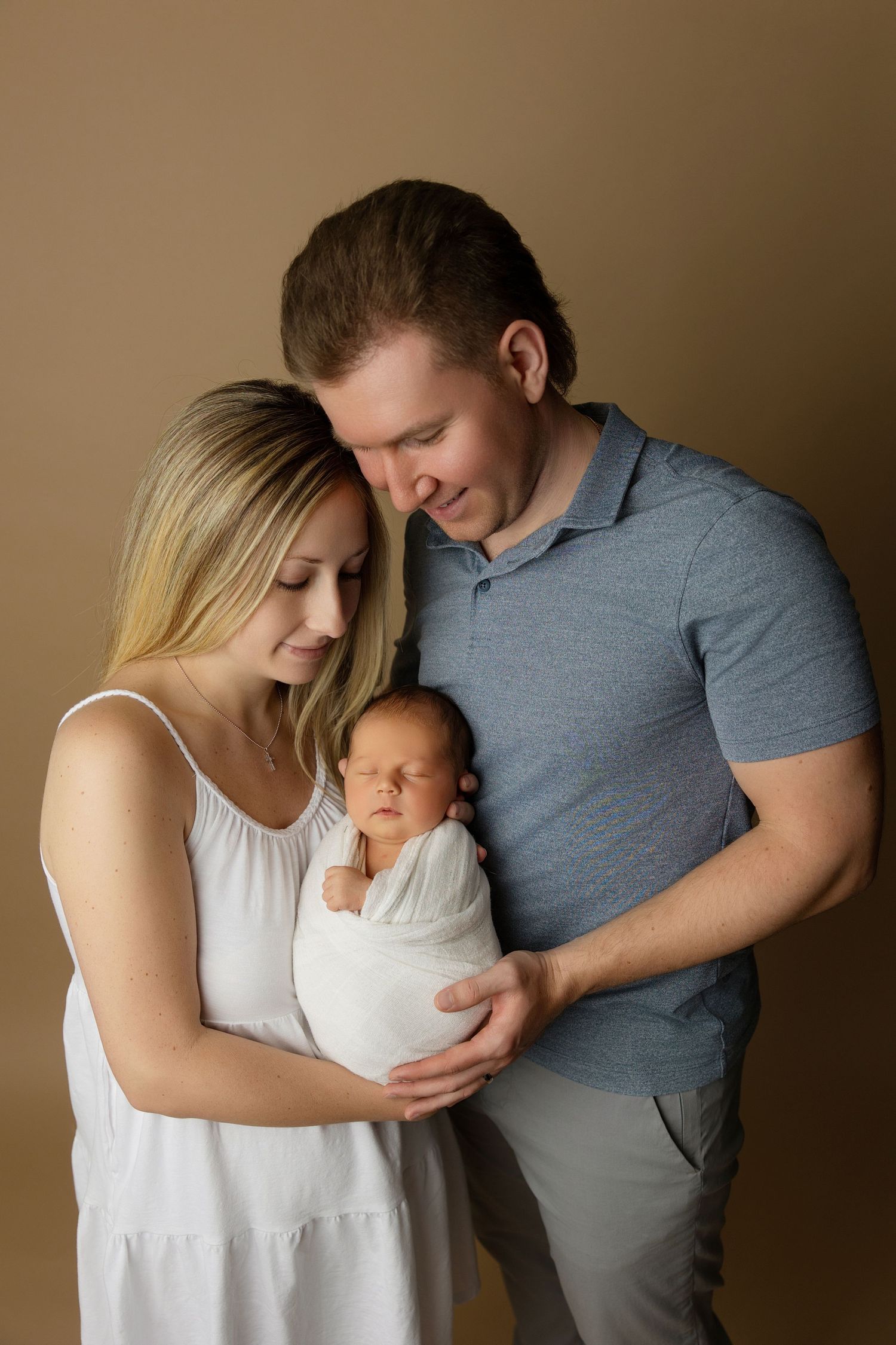 Intimate studio portrait of new parents with their newborn baby against neutral background.