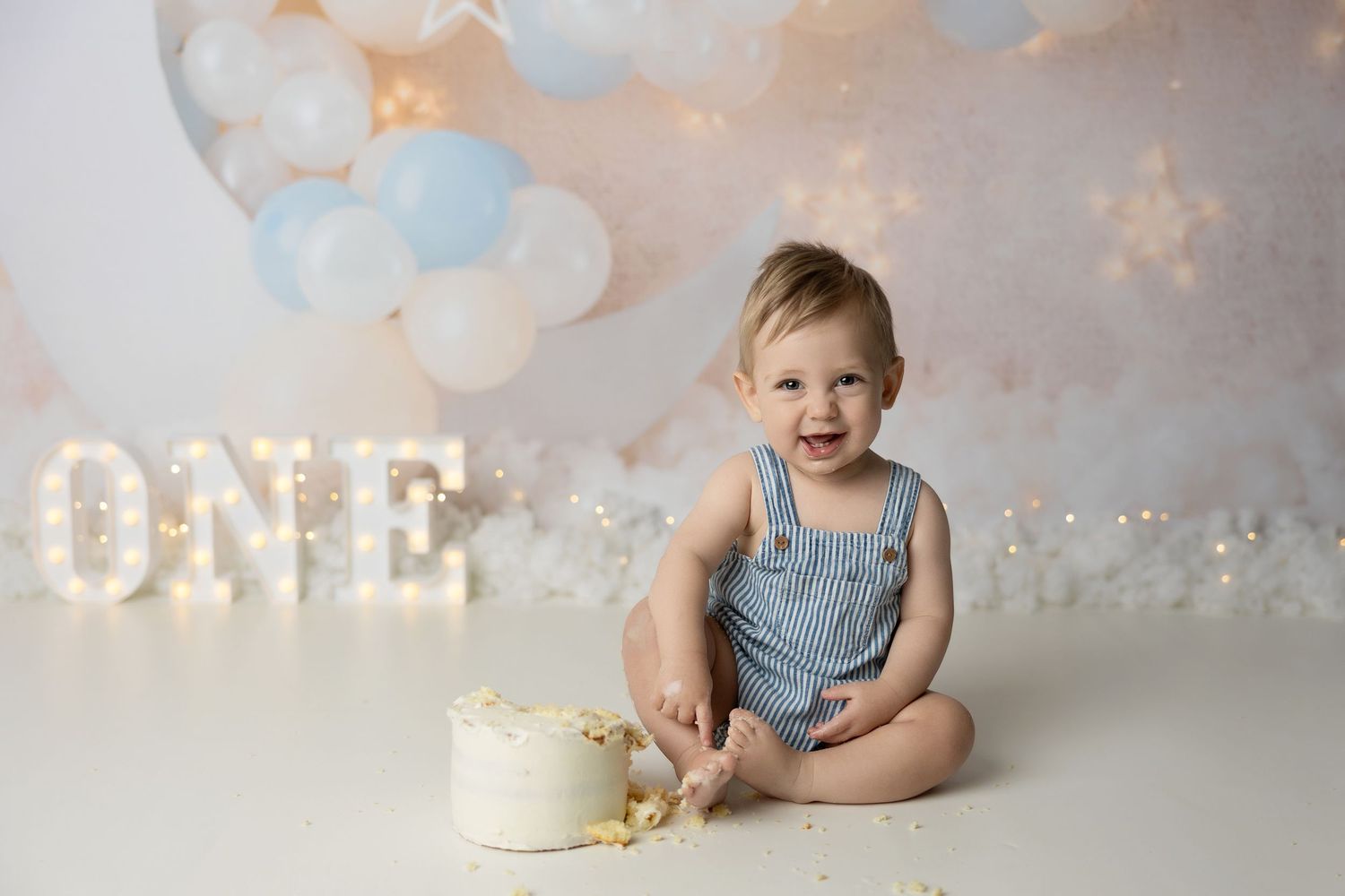 Cake smash photo session setup with a white cake on a rustic backdrop in soft lighting.