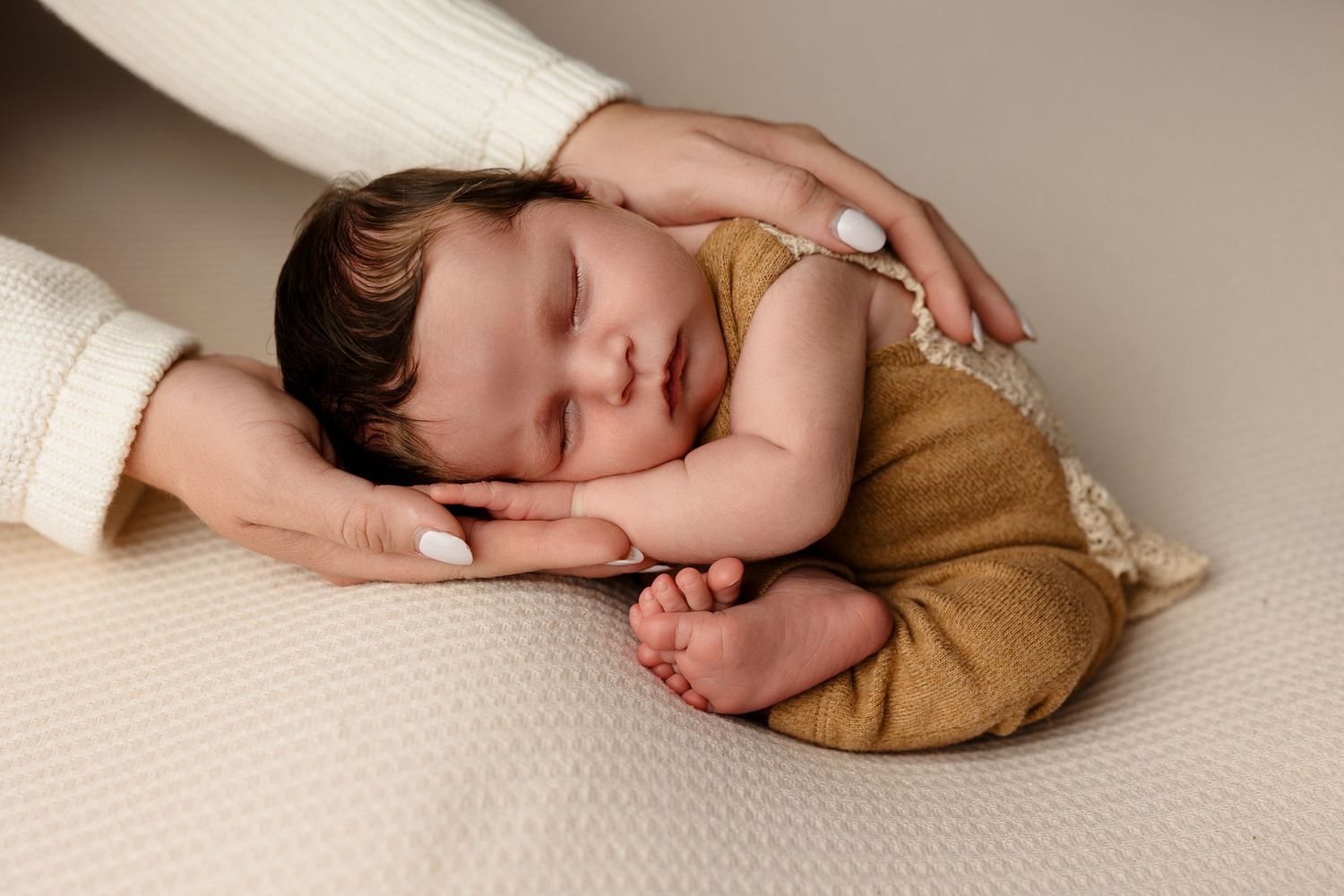 Baby sleeping peacefully in brown outfit on white textured surface.