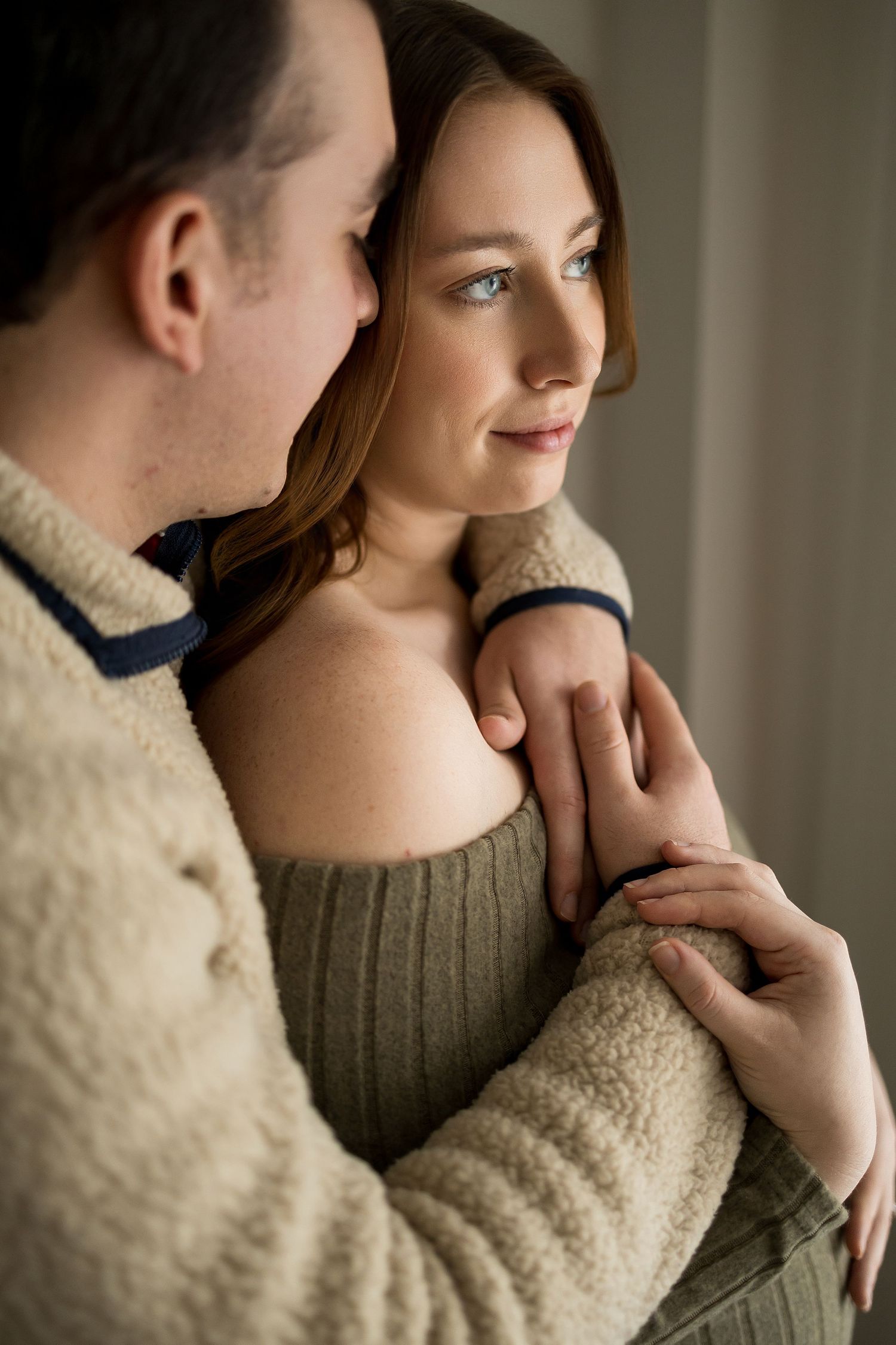 A tender moment captured between a couple during their maternity photoshoot near a window.