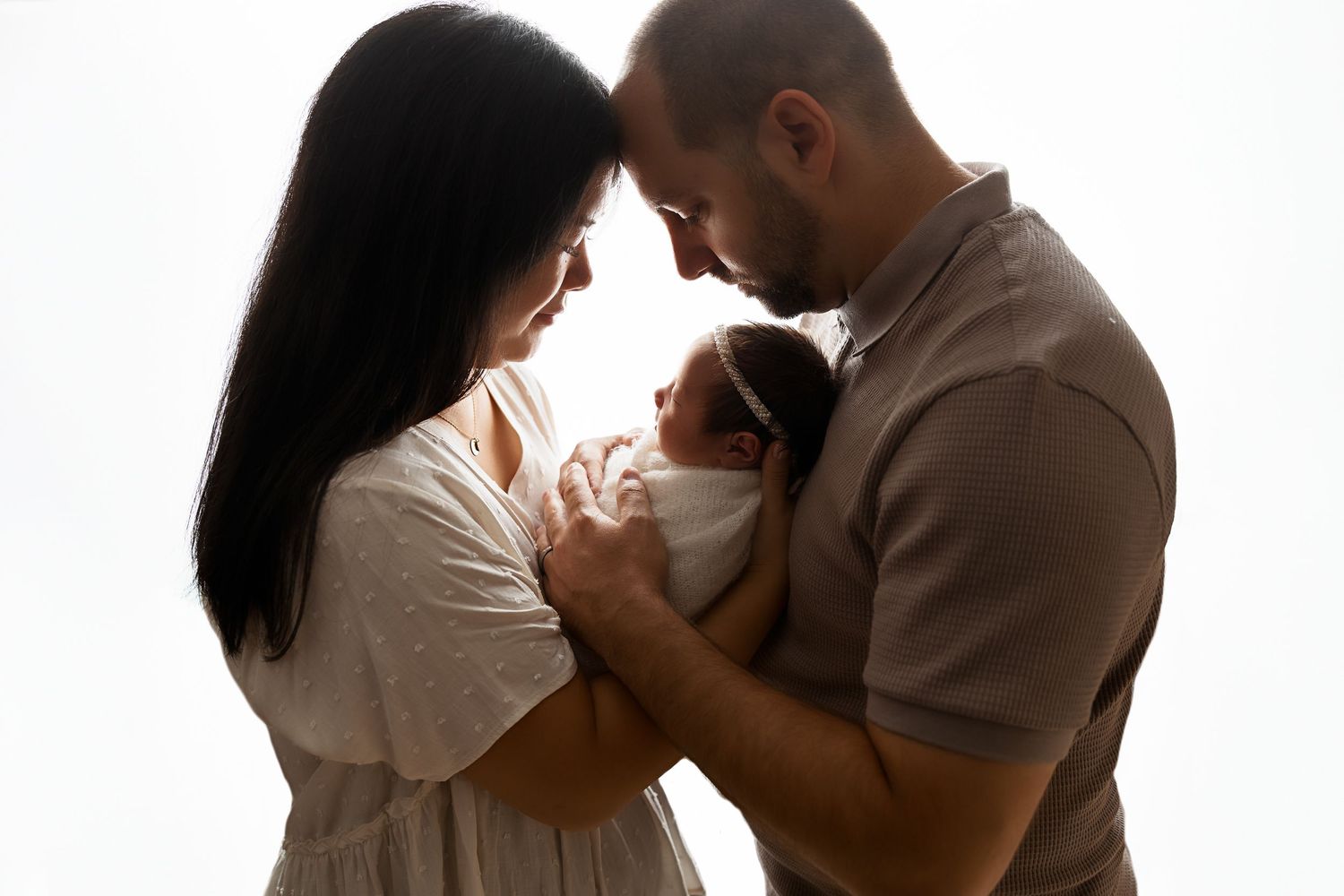 New parents cradling their newborn baby together in silhouette against white background.