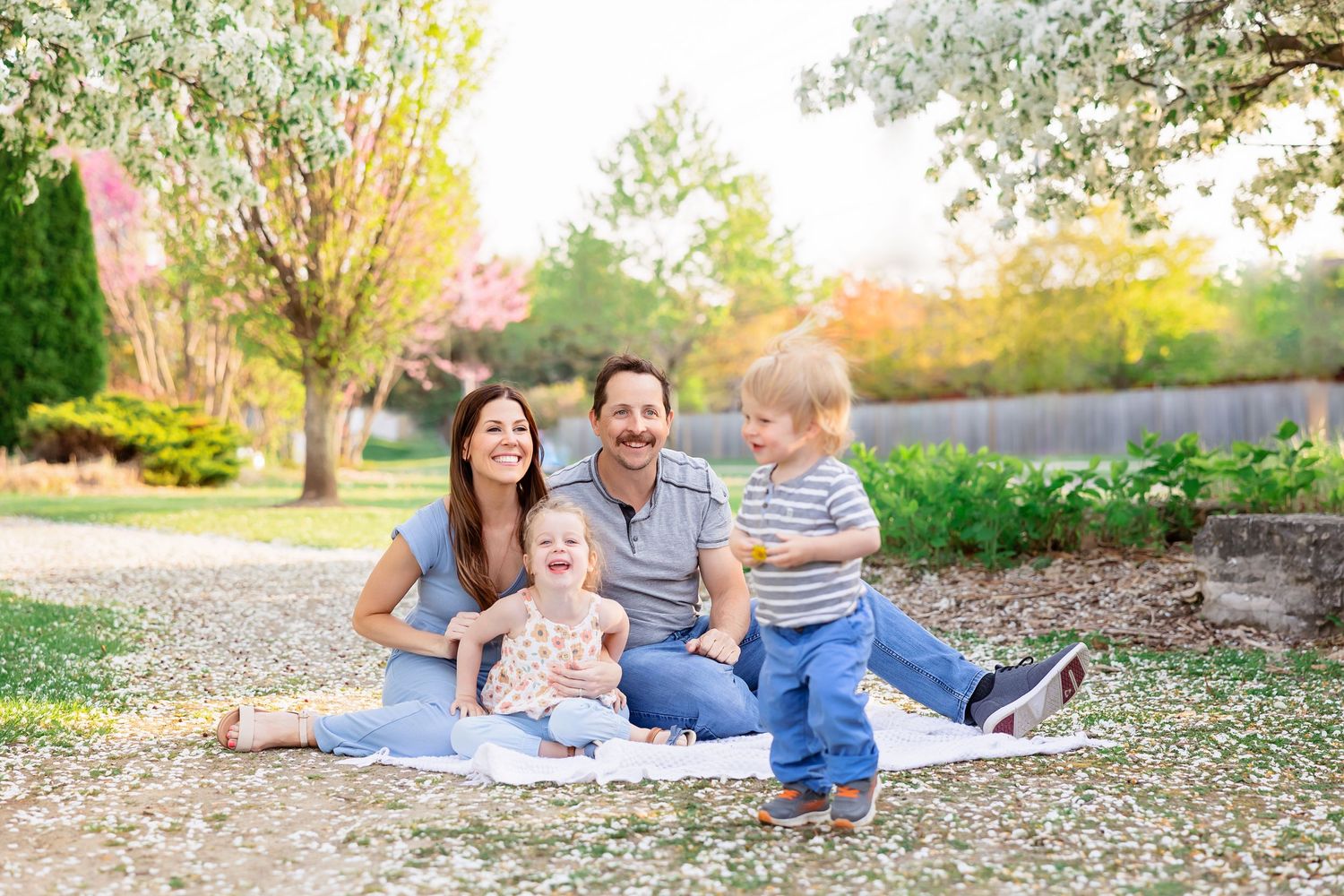 A family sits together on a blanket outdoors during golden hour in a park setting.