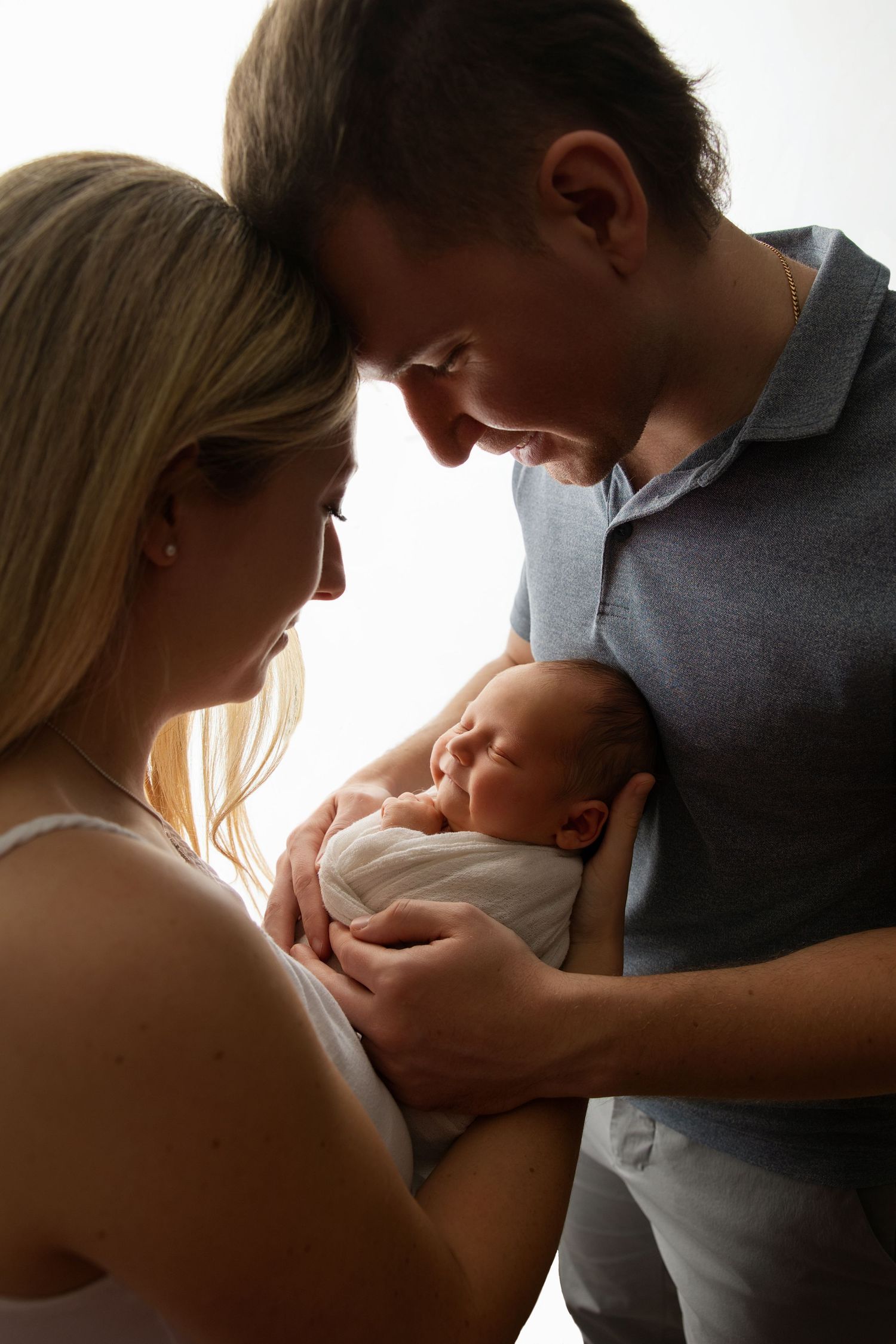 Parents sharing an intimate moment with their newborn baby against a bright background.