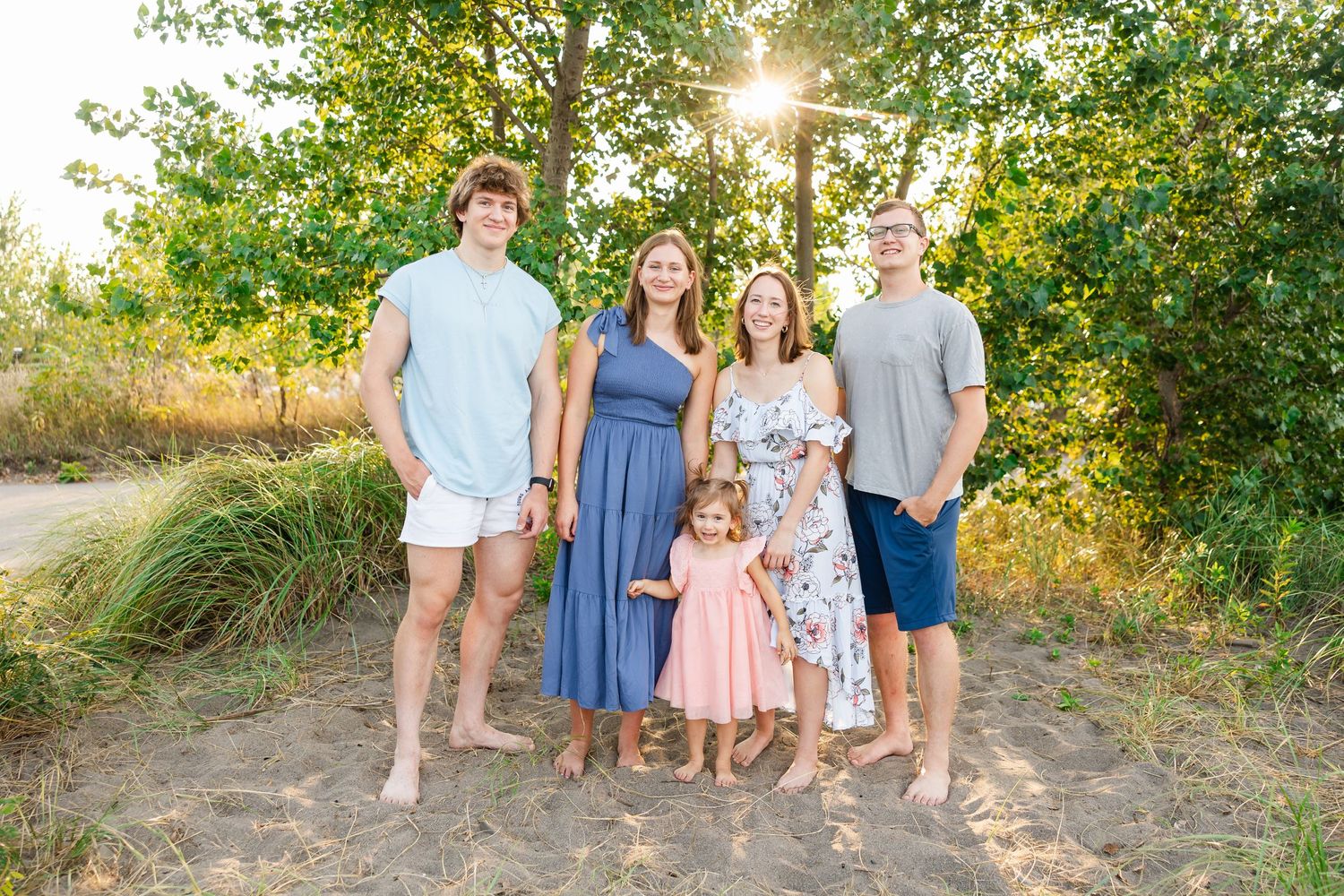 A group in coordinated blue and pink outfits poses together at sunset in a natural outdoor setting with golden sunlight.