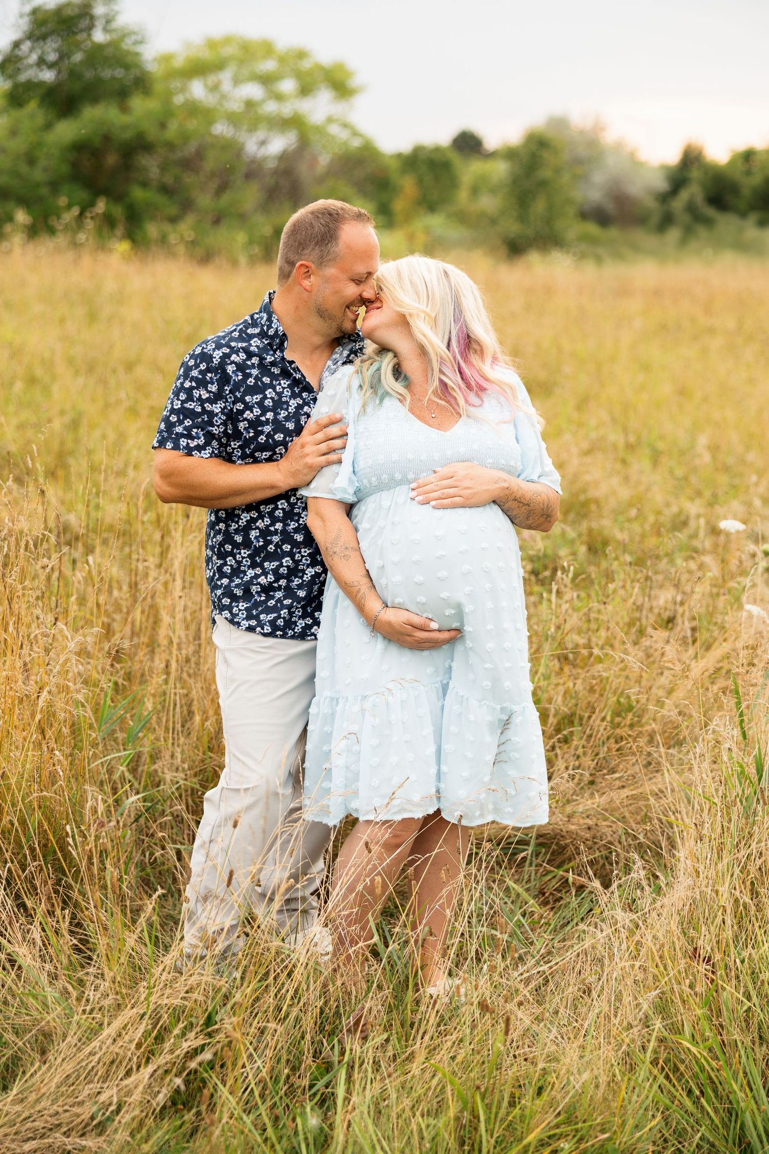 A couple embraces joyfully in a sun-drenched meadow filled with tall grass during a romantic photo session.