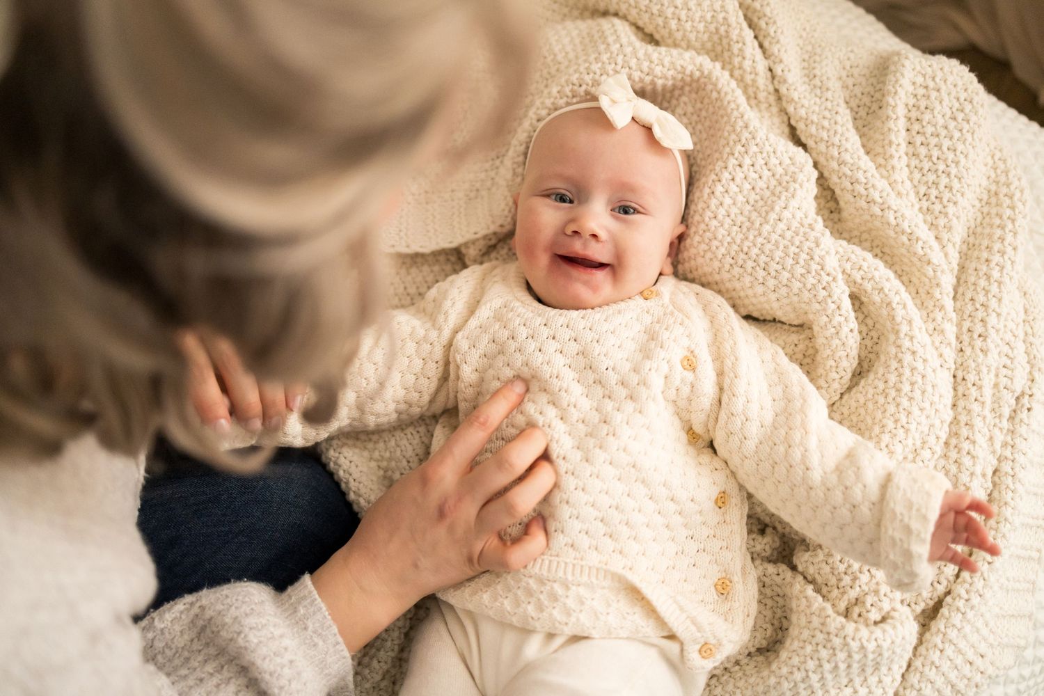Baby lying on cream knit blanket smiling and playing with hands in a series of candid moments.