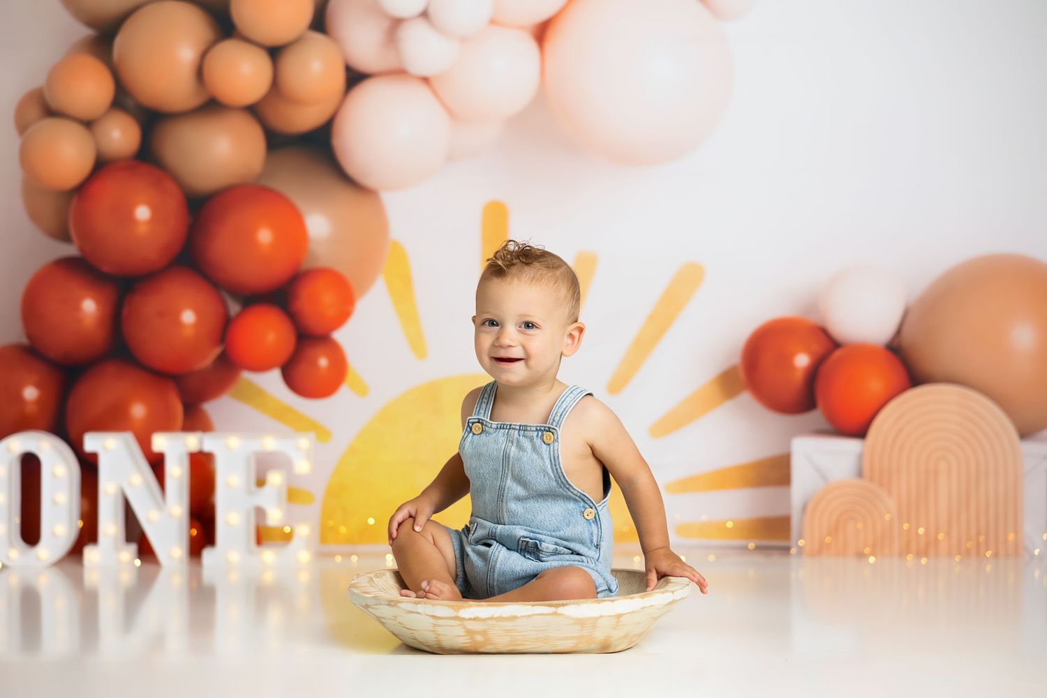 Celebratory first birthday scene with orange and white balloon arch and sunshine-themed backdrop.