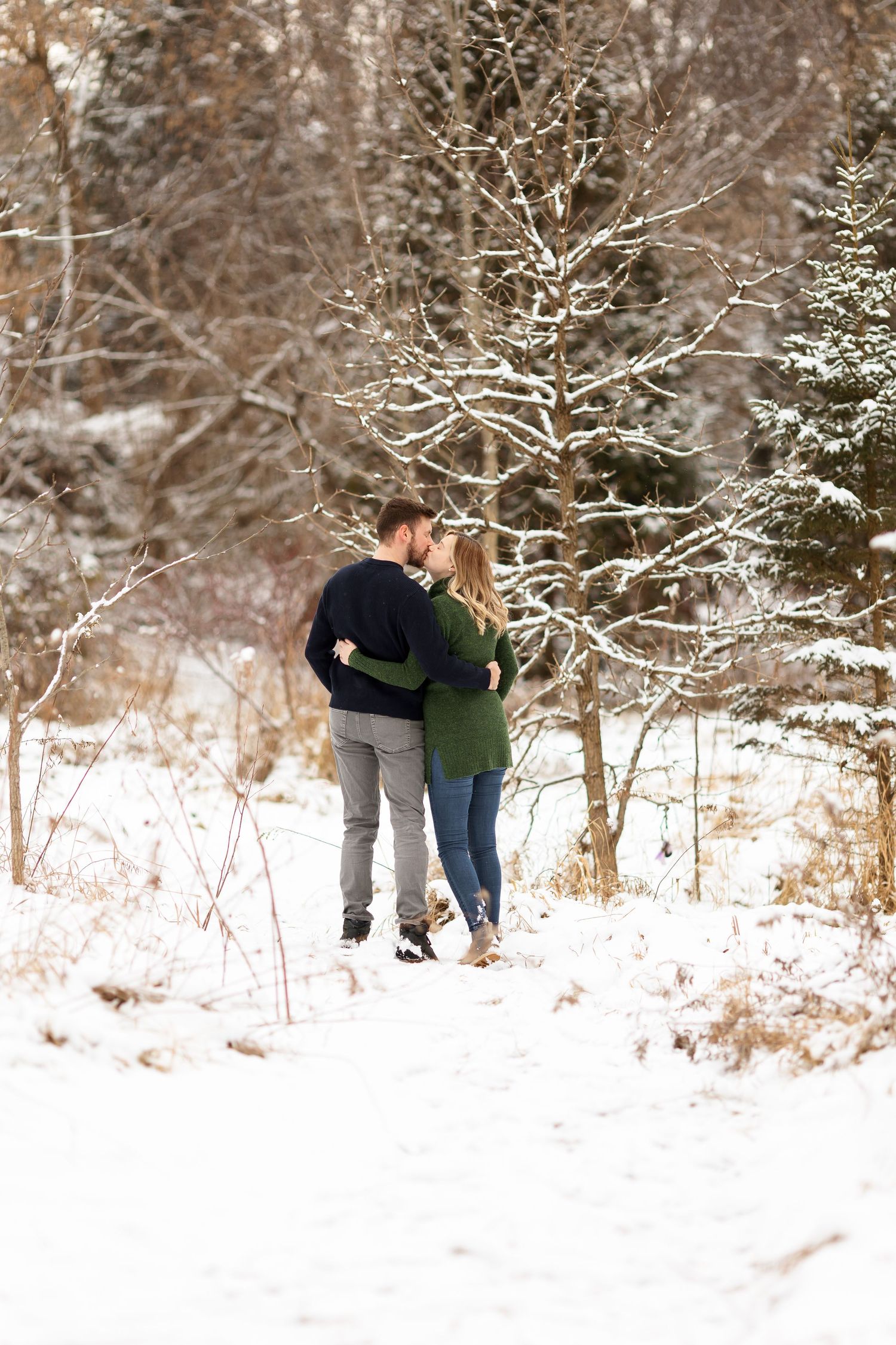 An intimate winter portrait of a couple among snow-covered trees.