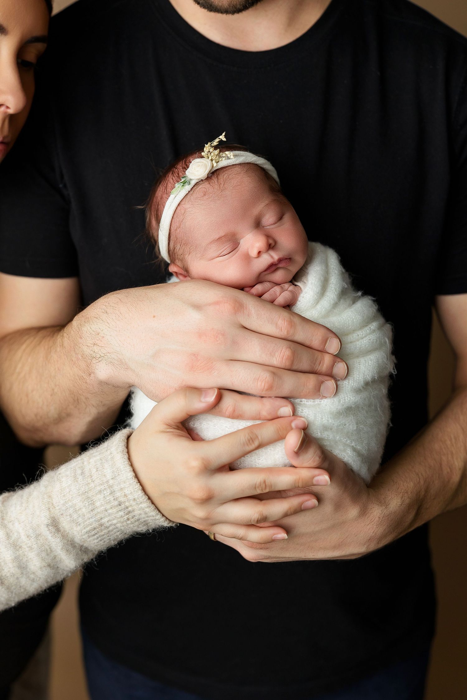 Swaddled sleeping newborn with delicate headband held in gentle embrace.