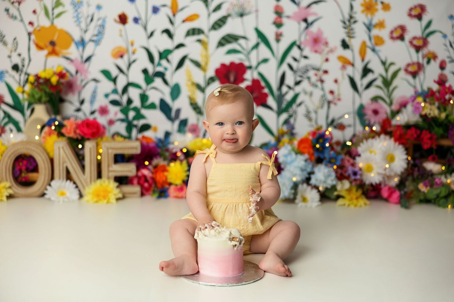 First birthday portrait with floral backdrop and gold 'ONE' lettering.