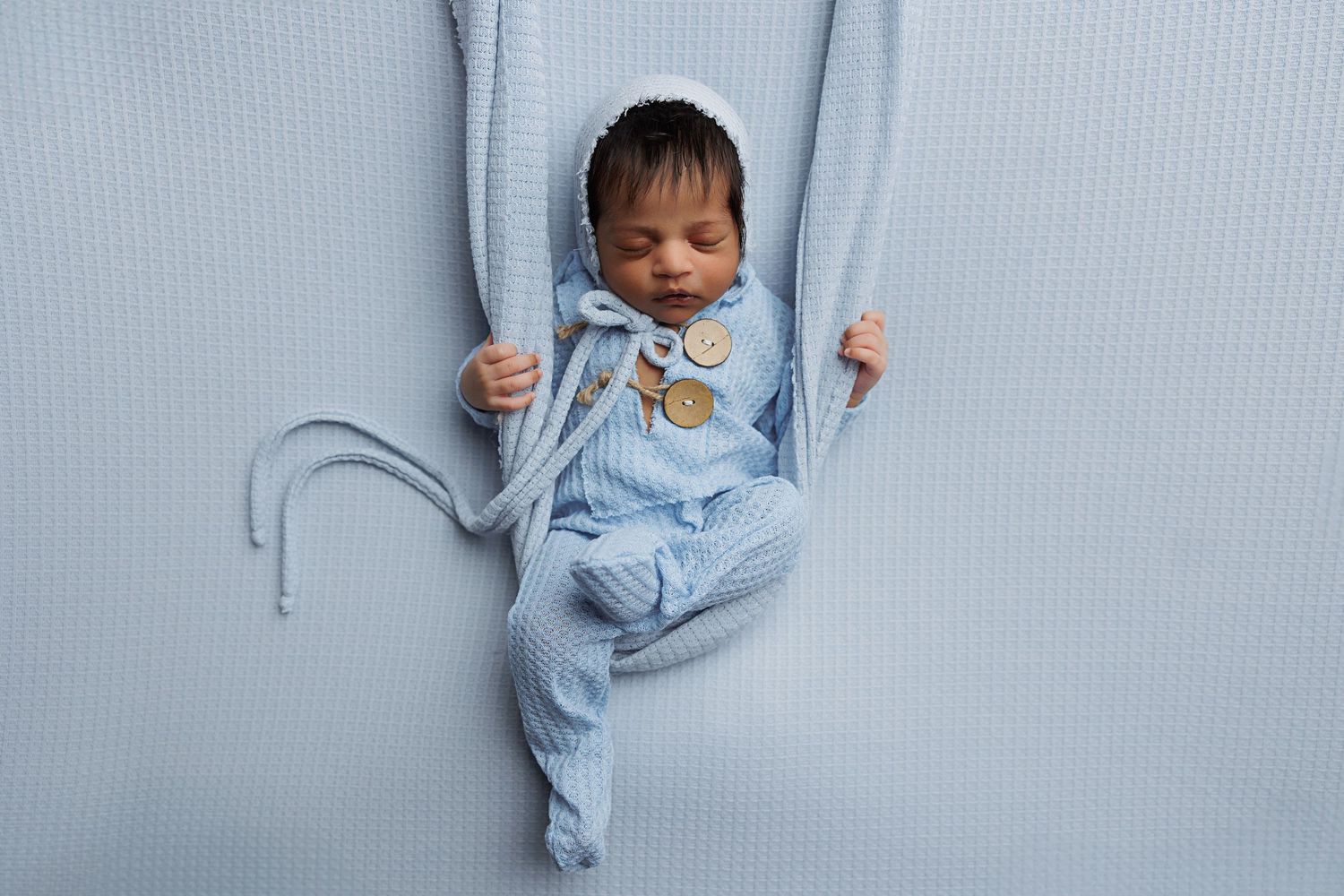 Newborn baby in light blue outfit during professional photo session.