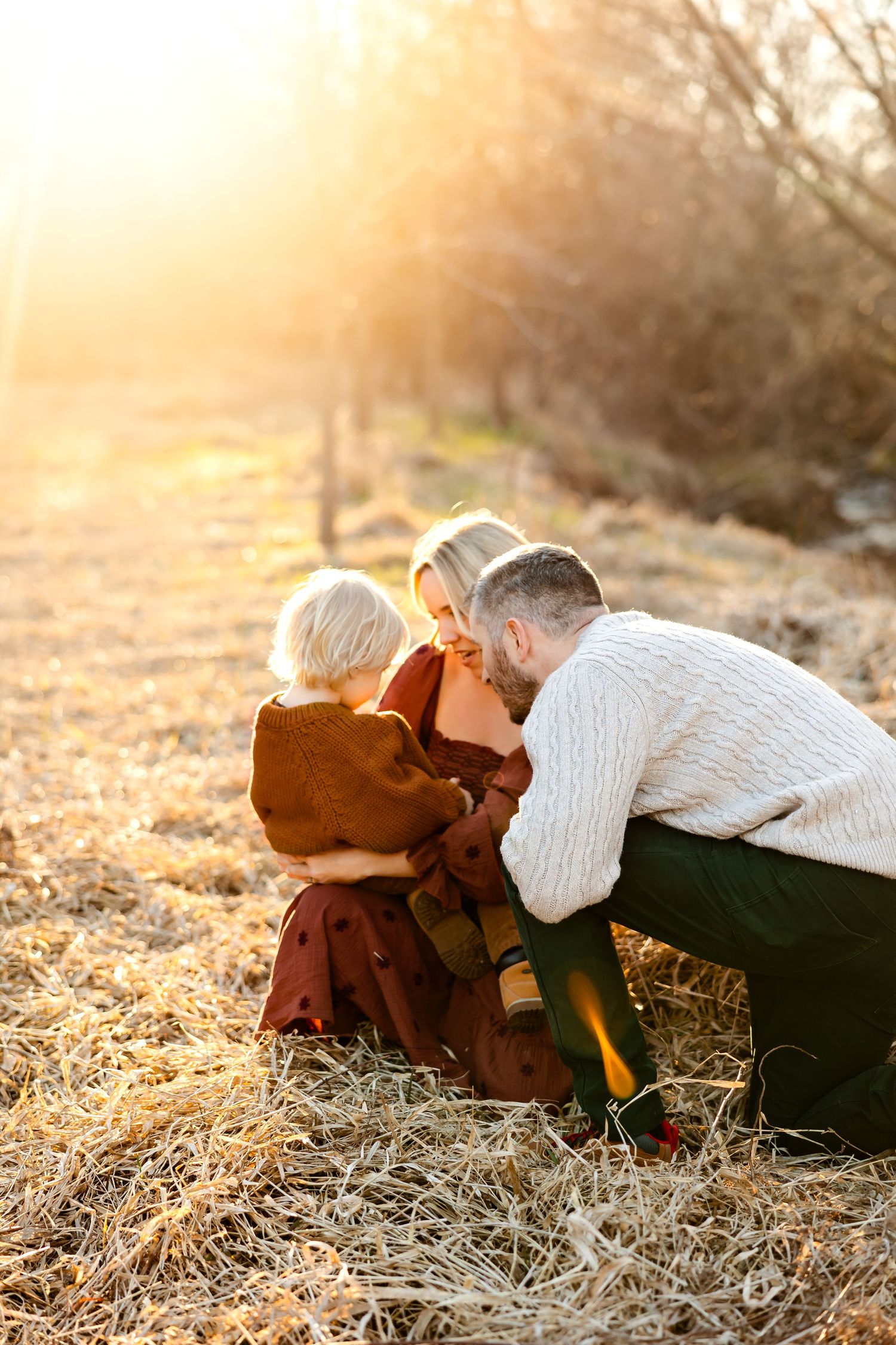 A tender family moment captured in warm sunset light on dried grass.