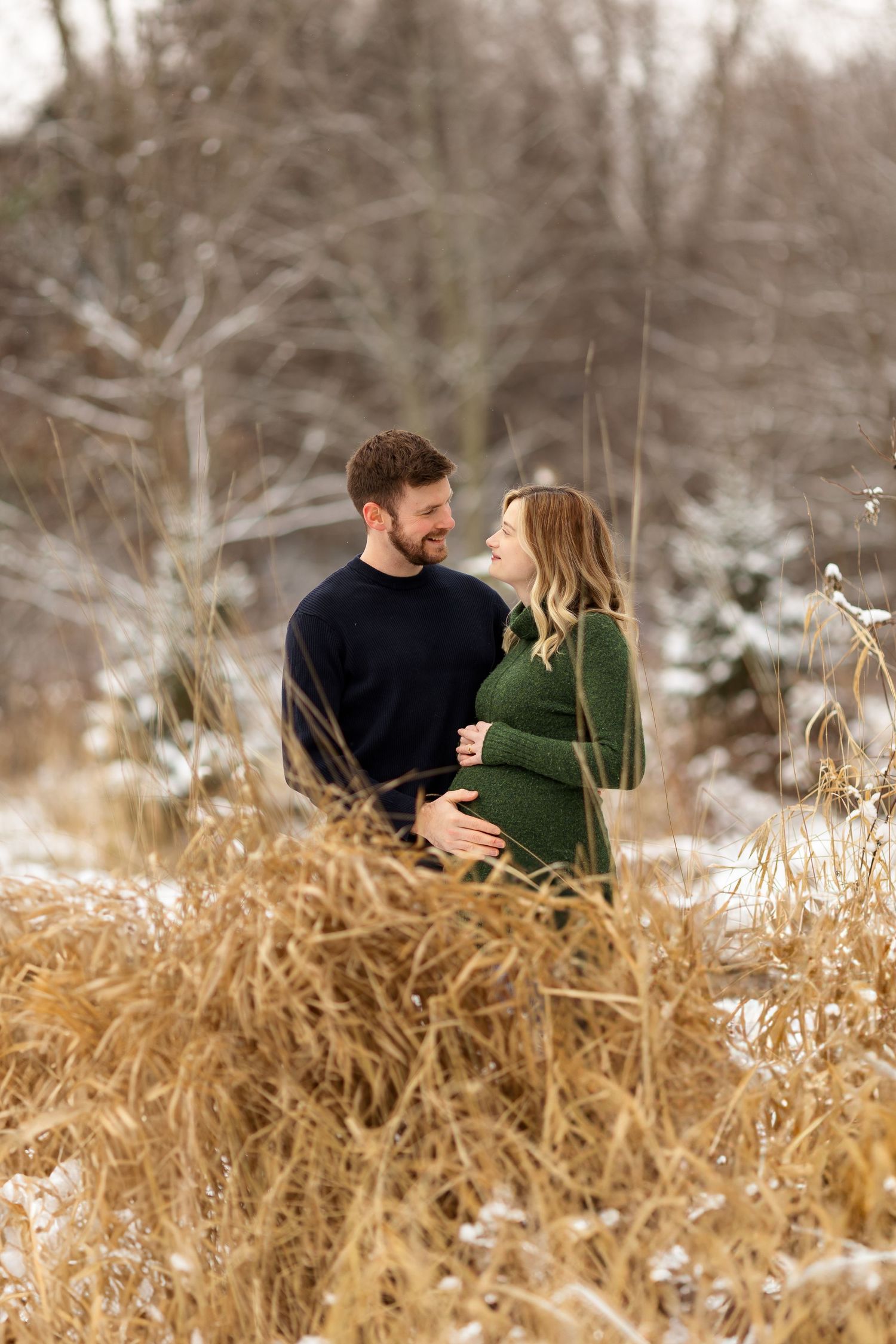Winter maternity photography session among golden dried grass and snowy landscape.