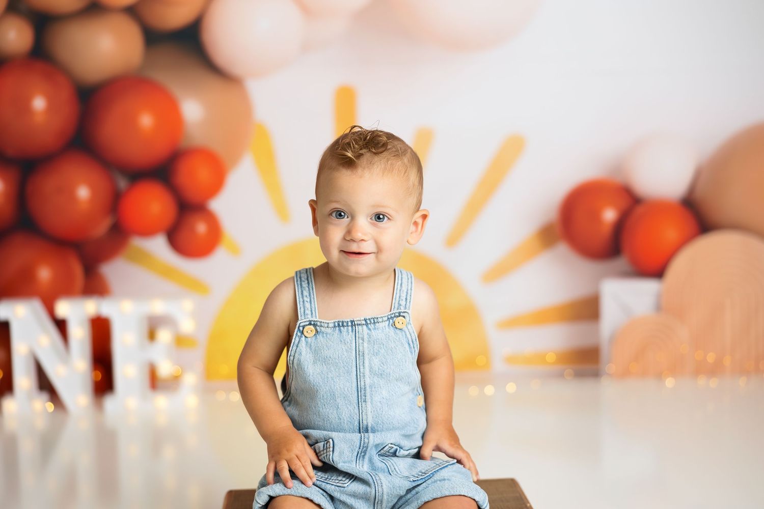 Birthday photo session with rustic wooden seat and festive balloon background.