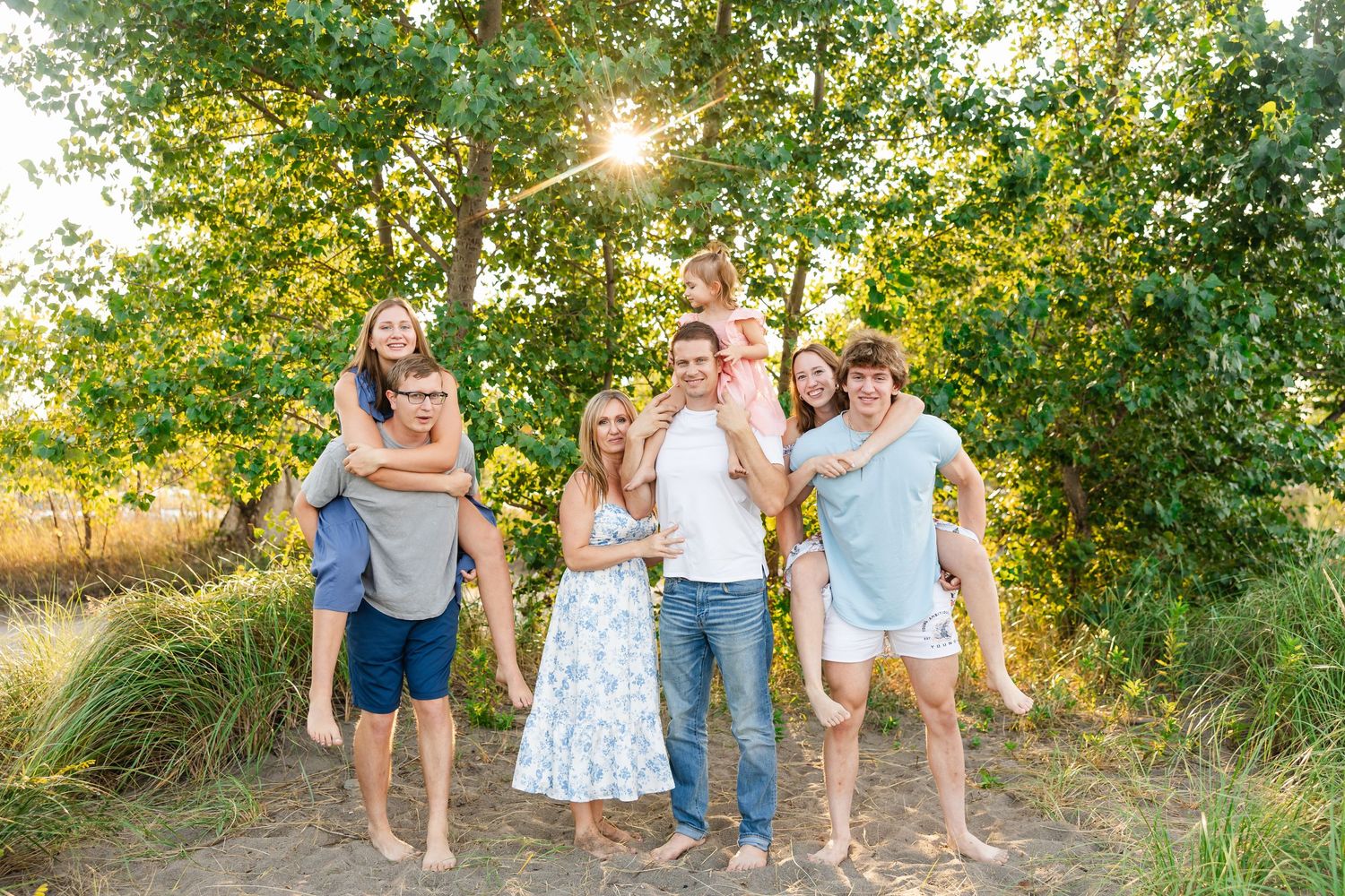 Happy group poses together at sunset in a natural outdoor setting with golden sunlight filtering through trees.