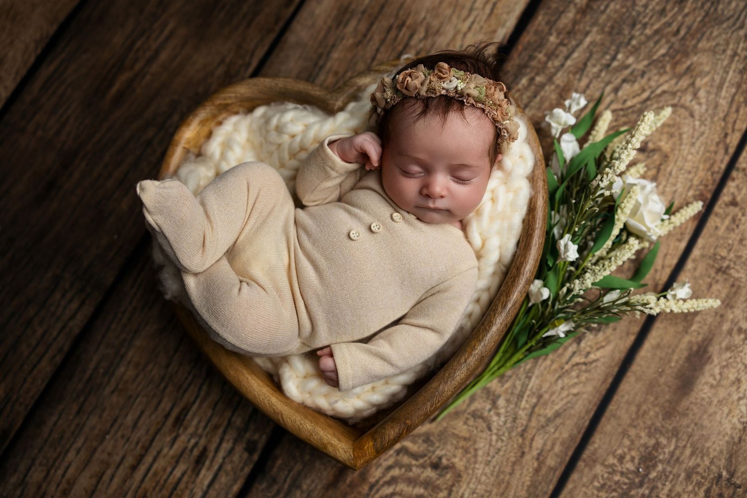 Sleeping newborn in minimal studio setup with wooden heart bowl and natural greenery accents