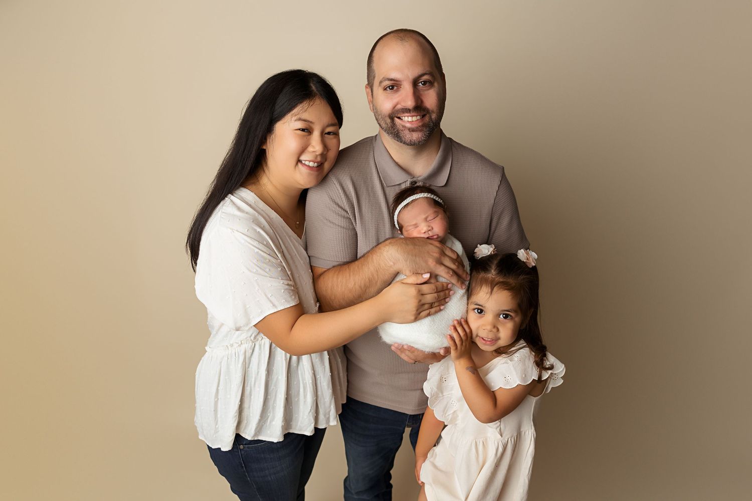A family of four poses together for a studio portrait against beige background.