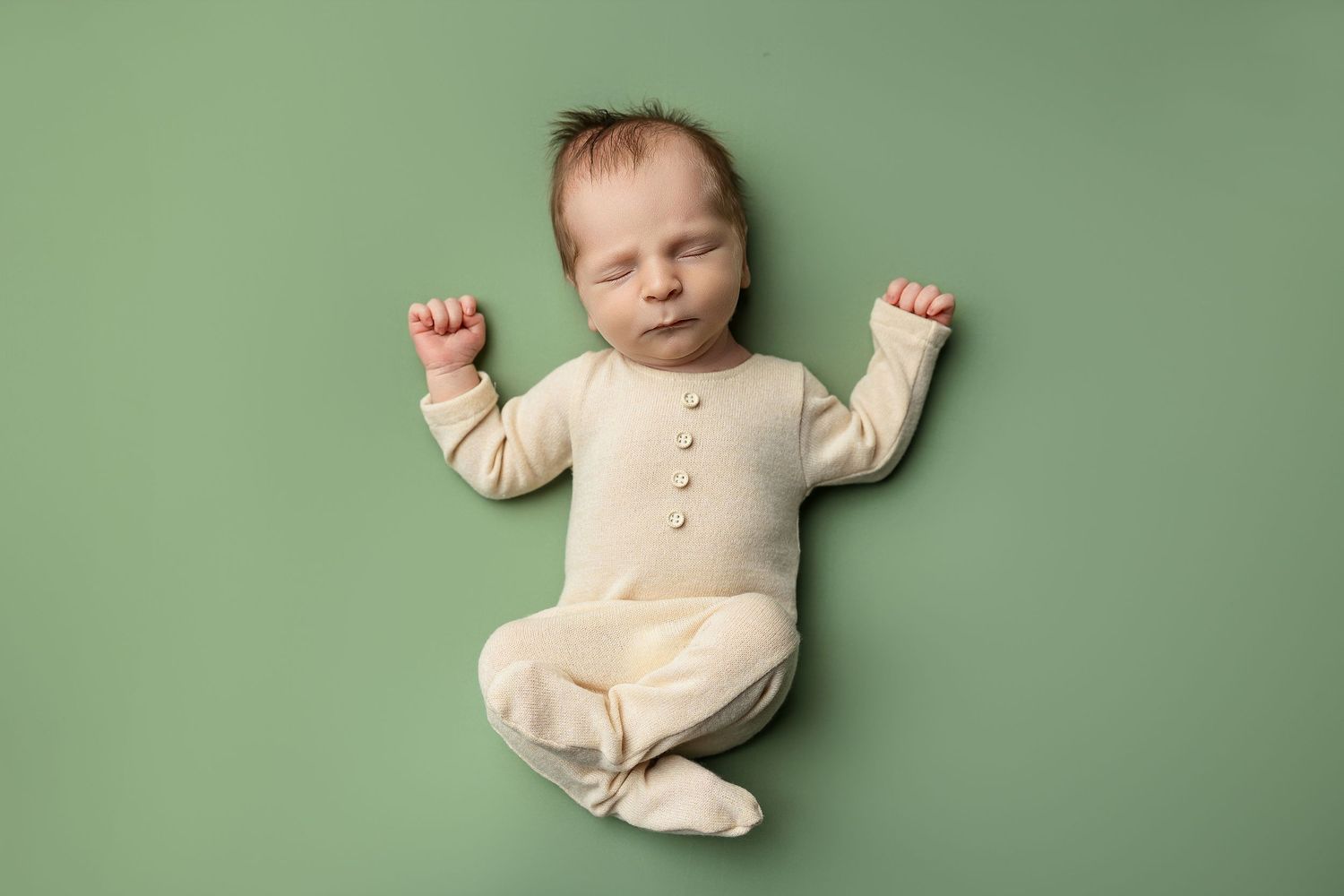 Newborn baby stretching limbs while lying on mint green backdrop.