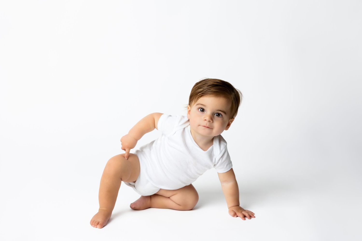 Baby in white shirt crawling on white studio backdrop.