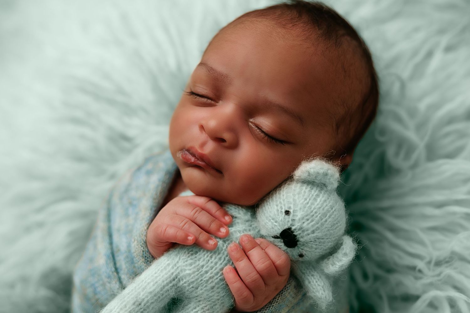 Peaceful sleeping baby holding soft gray teddy bear on mint green background.
