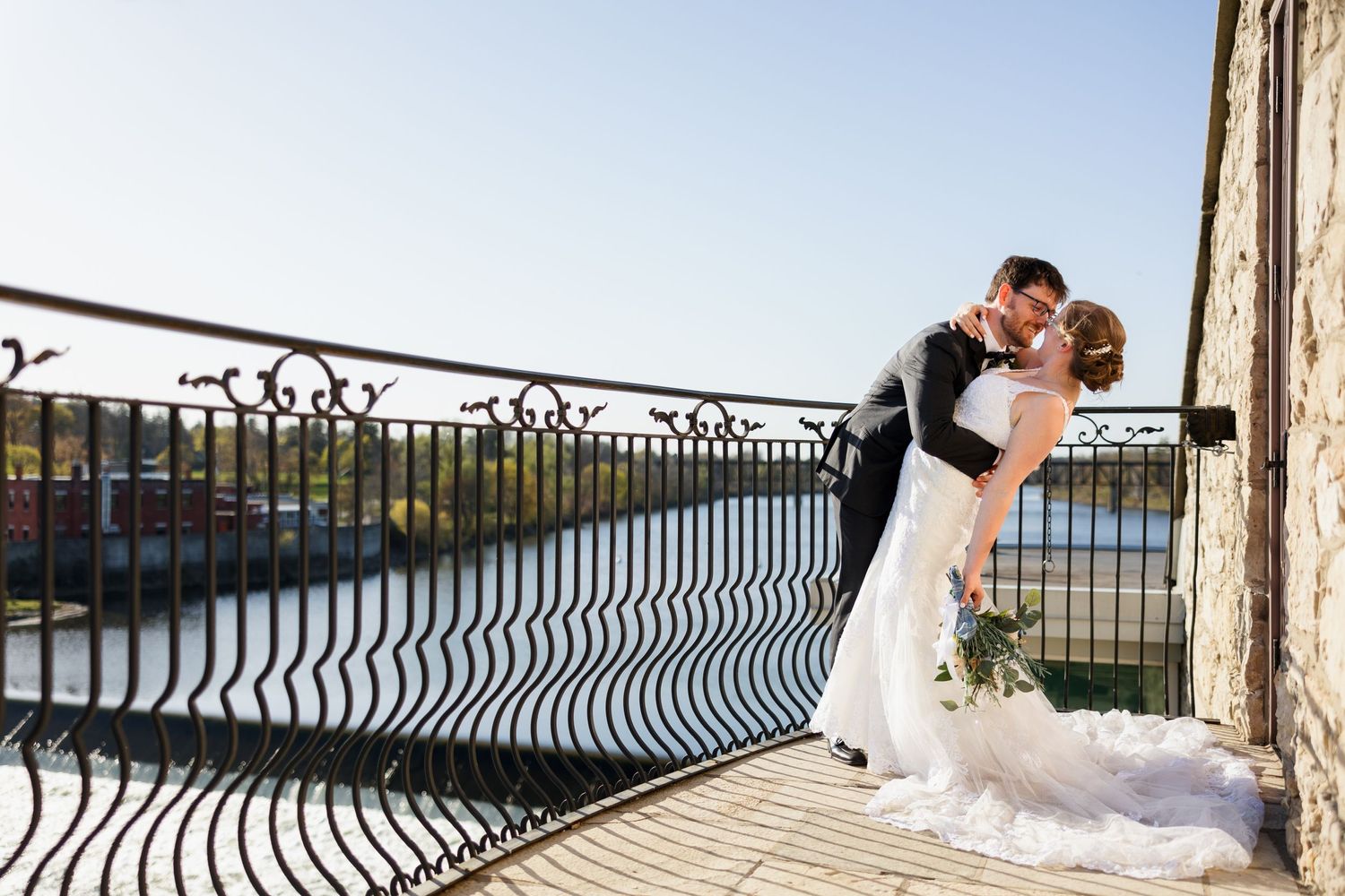 Romantic balcony portrait of newlyweds against iron railing with water view.