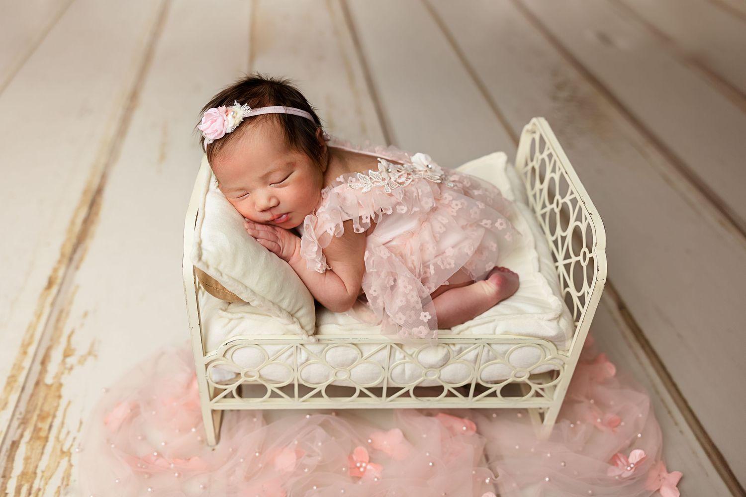 Newborn sleeping in vintage white metal bed with pink tulle and lace decorations.