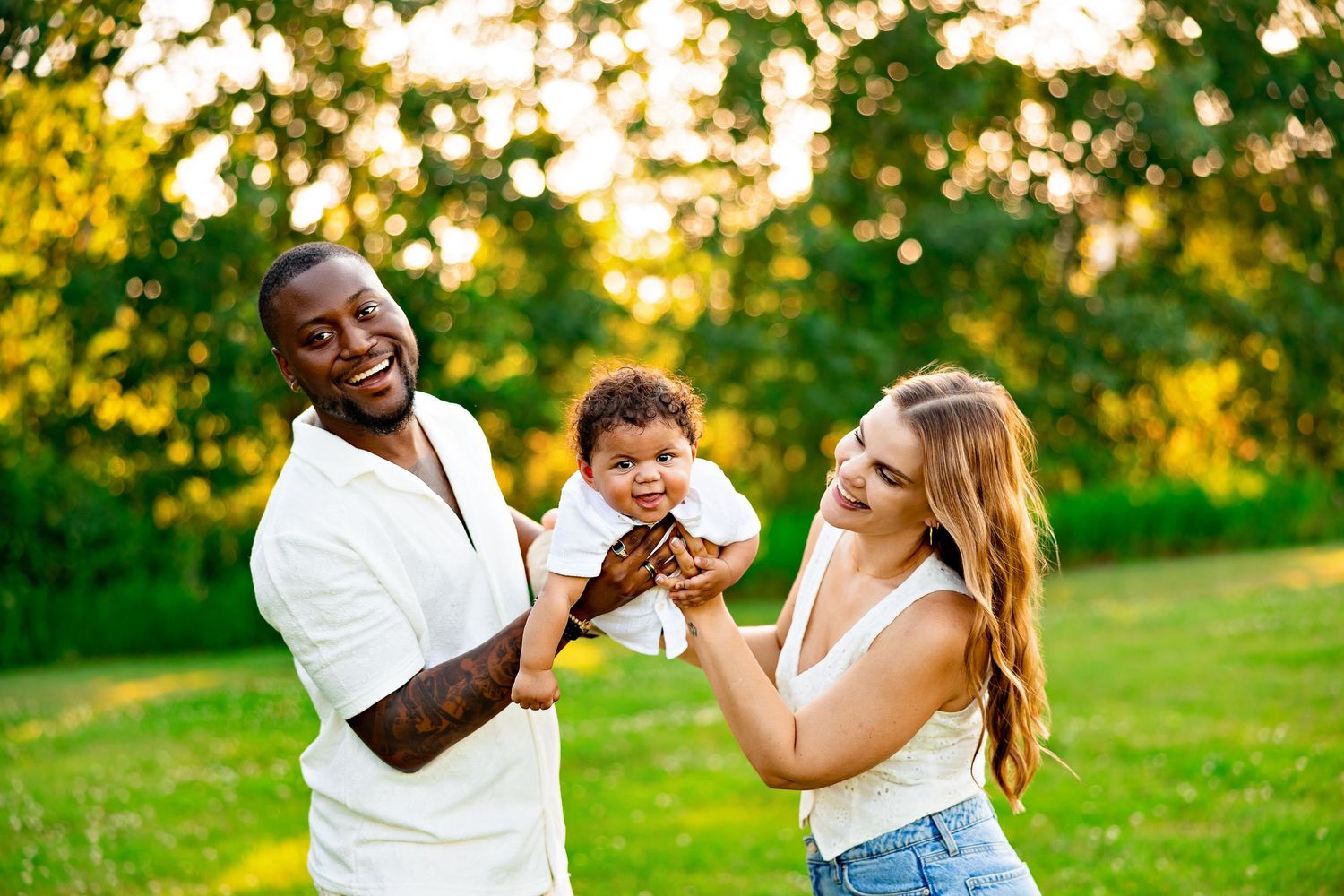 Happy family shares joyful moment with baby outdoors during golden sunset.