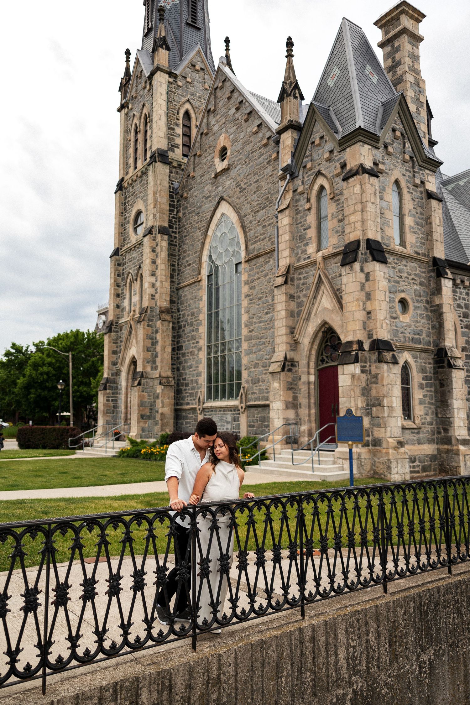 Couple embracing in front of a historic Gothic stone church with ornate architecture and iron fence.