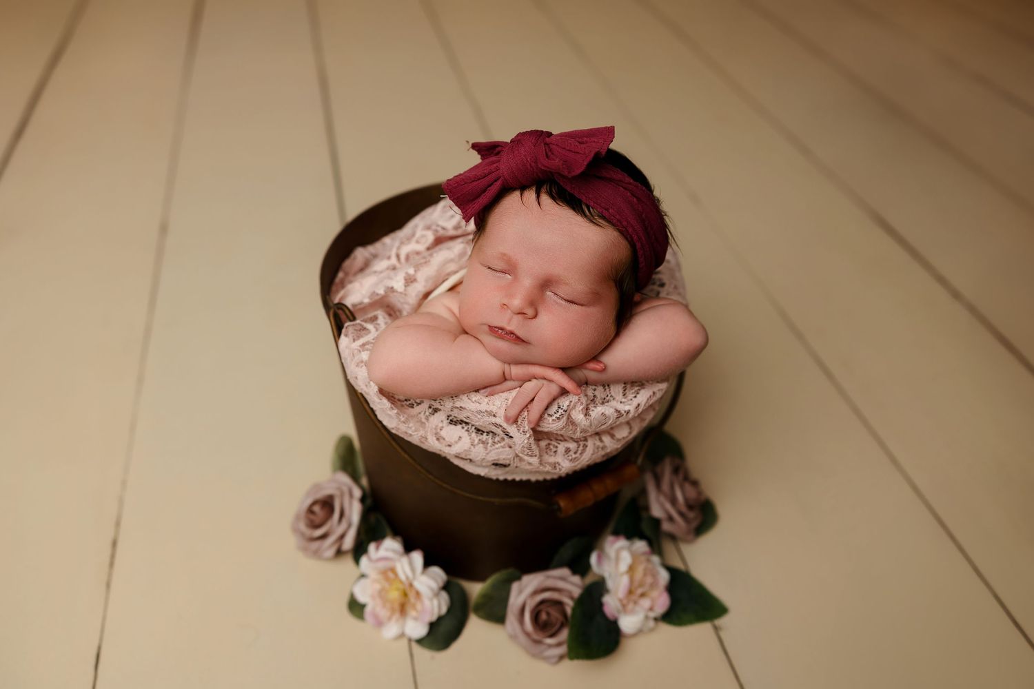 Newborn resting in wooden bowl decorated with pink roses and red headband.