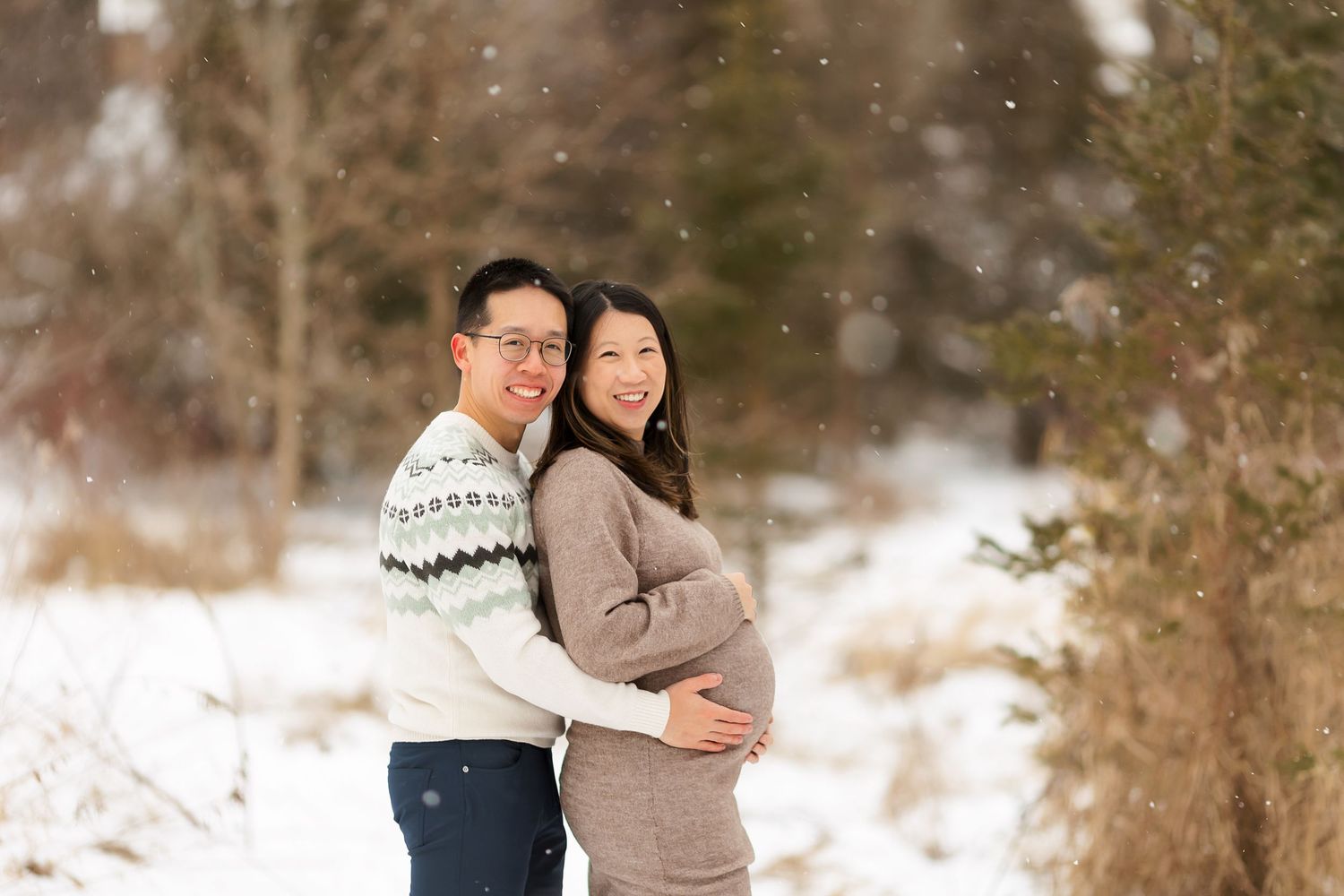 A winter maternity photo session in a snowy landscape with people embracing.